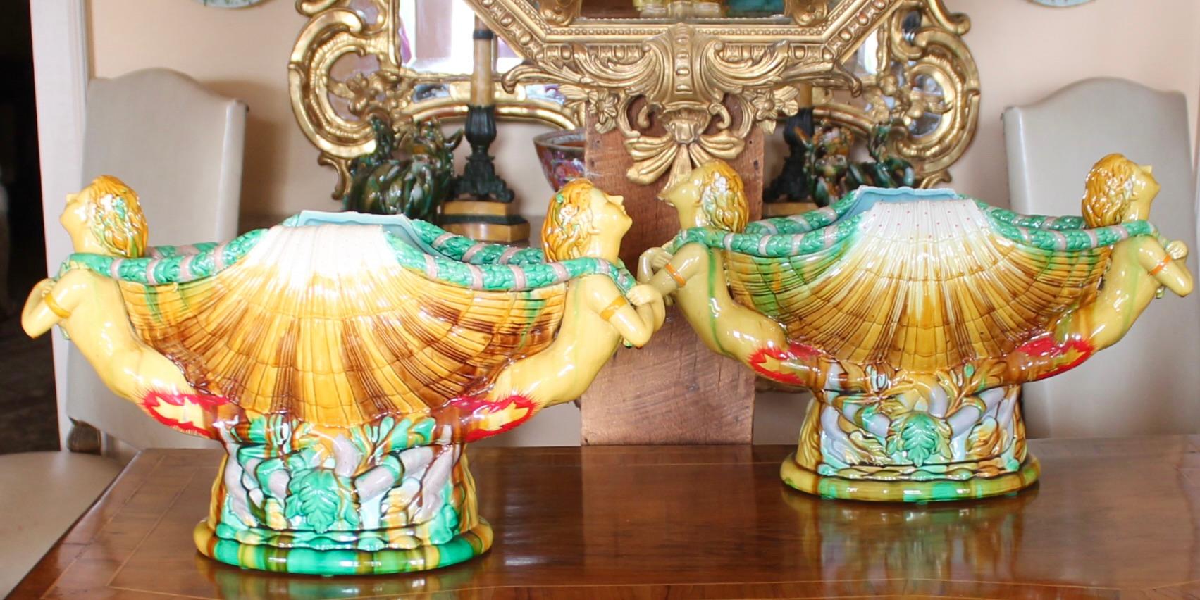 After a 19th century Minton majolica design, a fine of pair exuberantly formed  vessels, richly colored in ochre, bright green, light blue and red, the tails of the mermaids intertwine around the base of the composition. The seashell is multihued