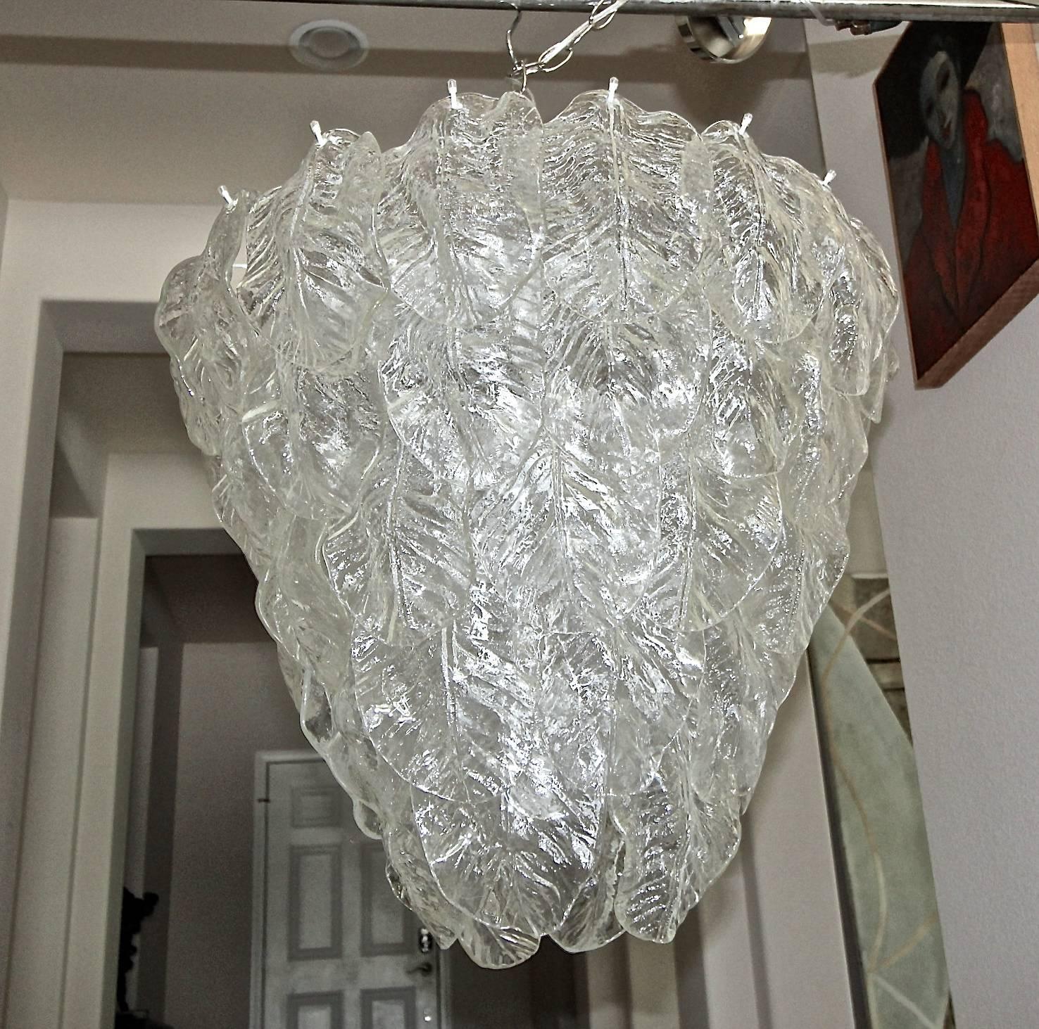 Pair (or sold individually) large Murano chandeliers each with nine-lights and five rows of clear textured glass leaves. Each uses nine 40-watt candelabra size bulbs. The Murano glass leaves are vintage from the 1960s, the white metal frames are