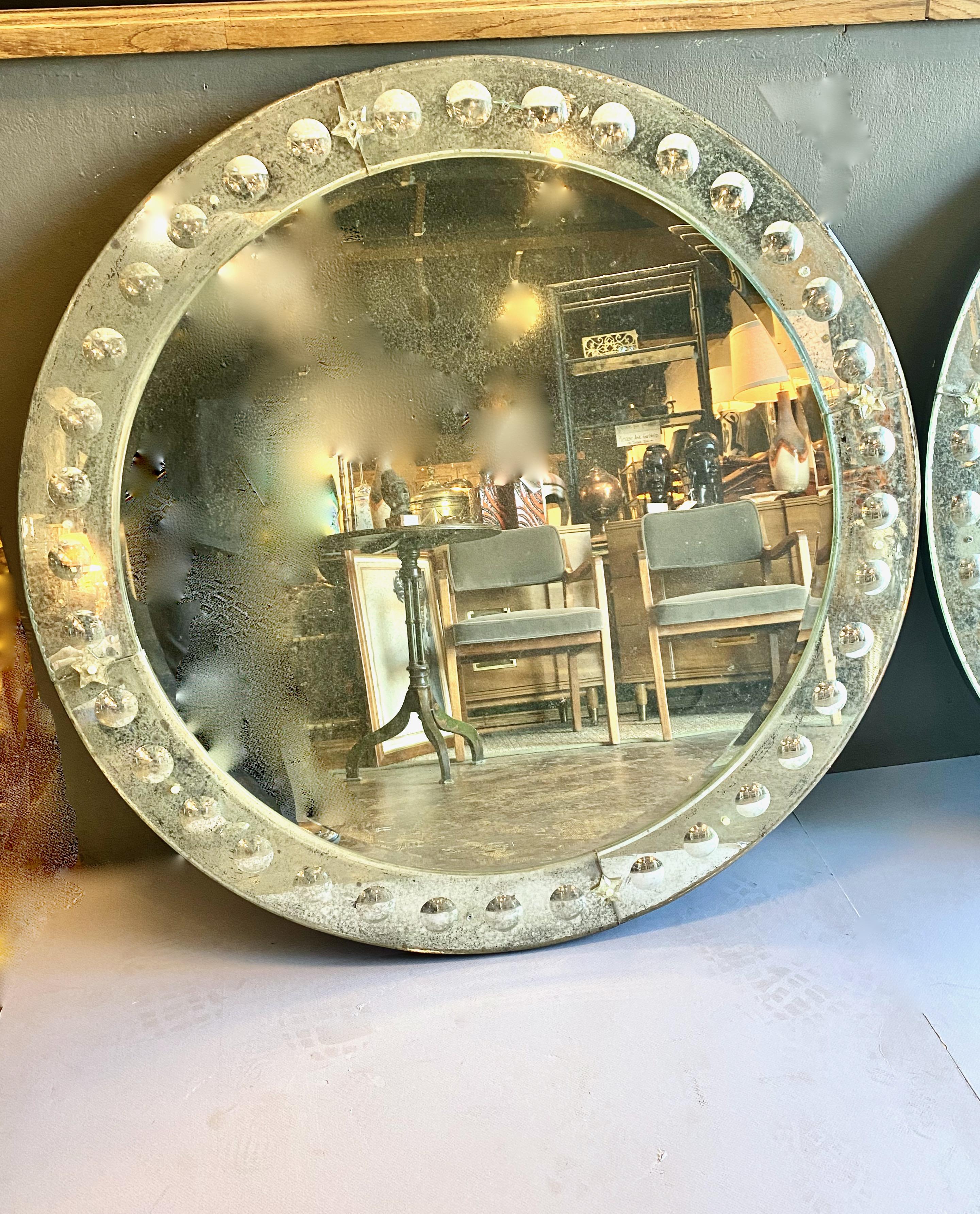 This is a spectacular pair of mid-20th century 40 inch diameter mercury glass mirrors. The central round section is surround by a deep beveled glass frame detailed with large hollowed out rondelles. The mercury glass has acquired a rich hazing which
