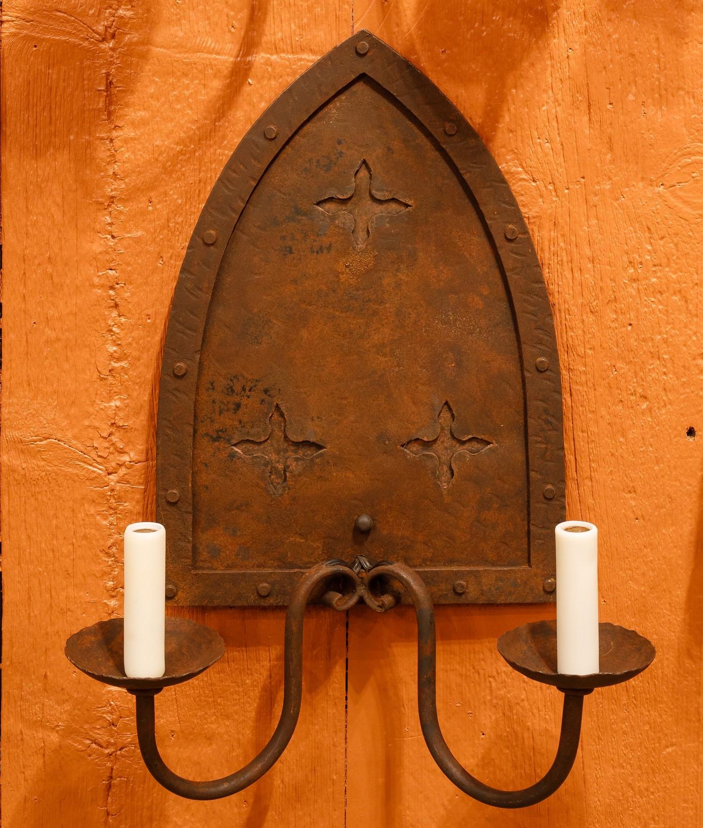 This hand-made pair of sconces has a simple and classic Gothic style.  The tall sconces have two arms that are situated so that they do not protrude too far from wall.  The hand-finished iron has a warm brown finish.  The finish could be adjusted to
