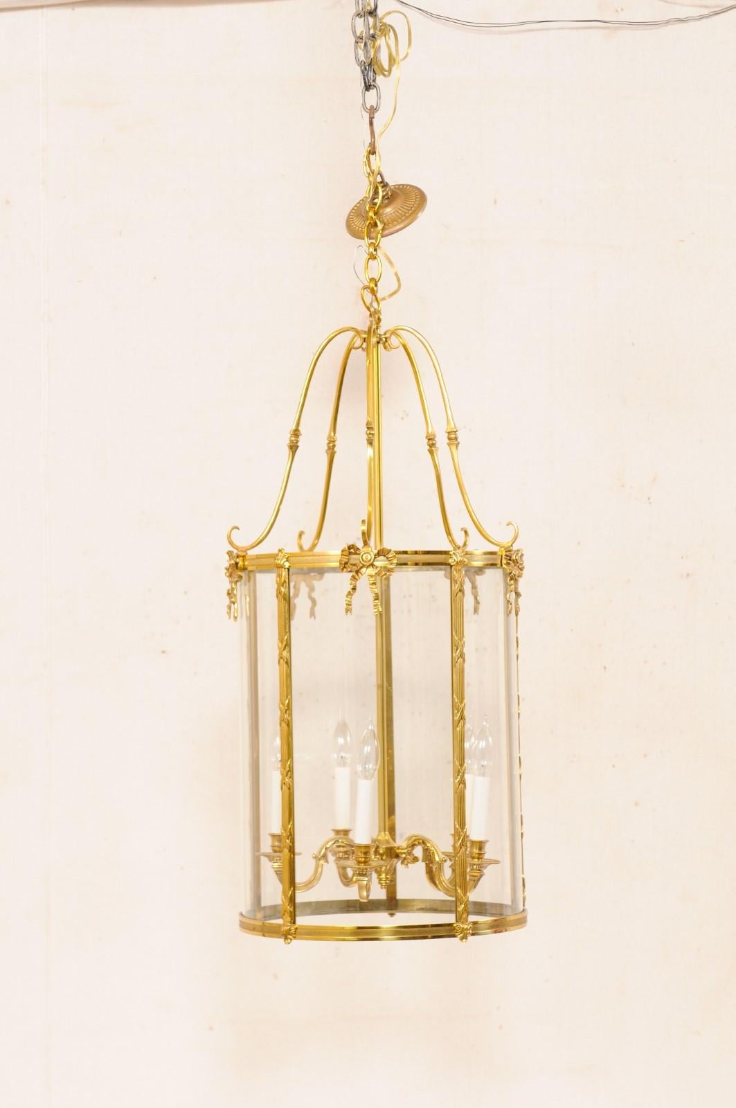 An English pair of large-size Adam style 5-light hanging brass lanterns. This vintage pair of lanterns from England, with their suspended domed-tops and tubular shaped bodies, have brass armature, with circular convex glass panels about the