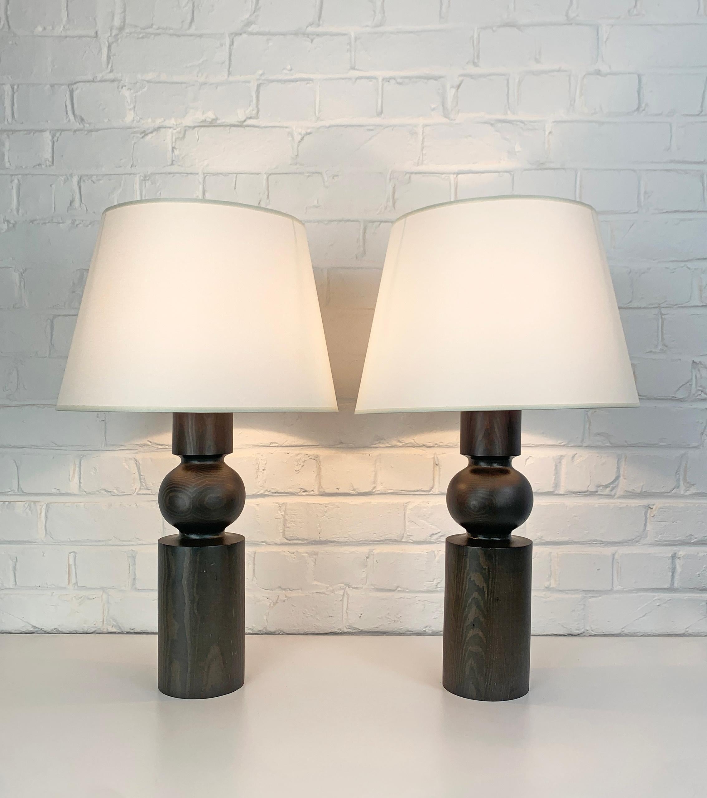A pair of sculptural table lamps. Lamp foots in turned pine wood, dark stained. 

Designed by Uno Kristiansson, for Luxus, Sweden, 1970s. Both are punchmarked Luxus - made in Sweden. 

For E26/27 bulbs. Work on 110v and on 220v. EU plug can be