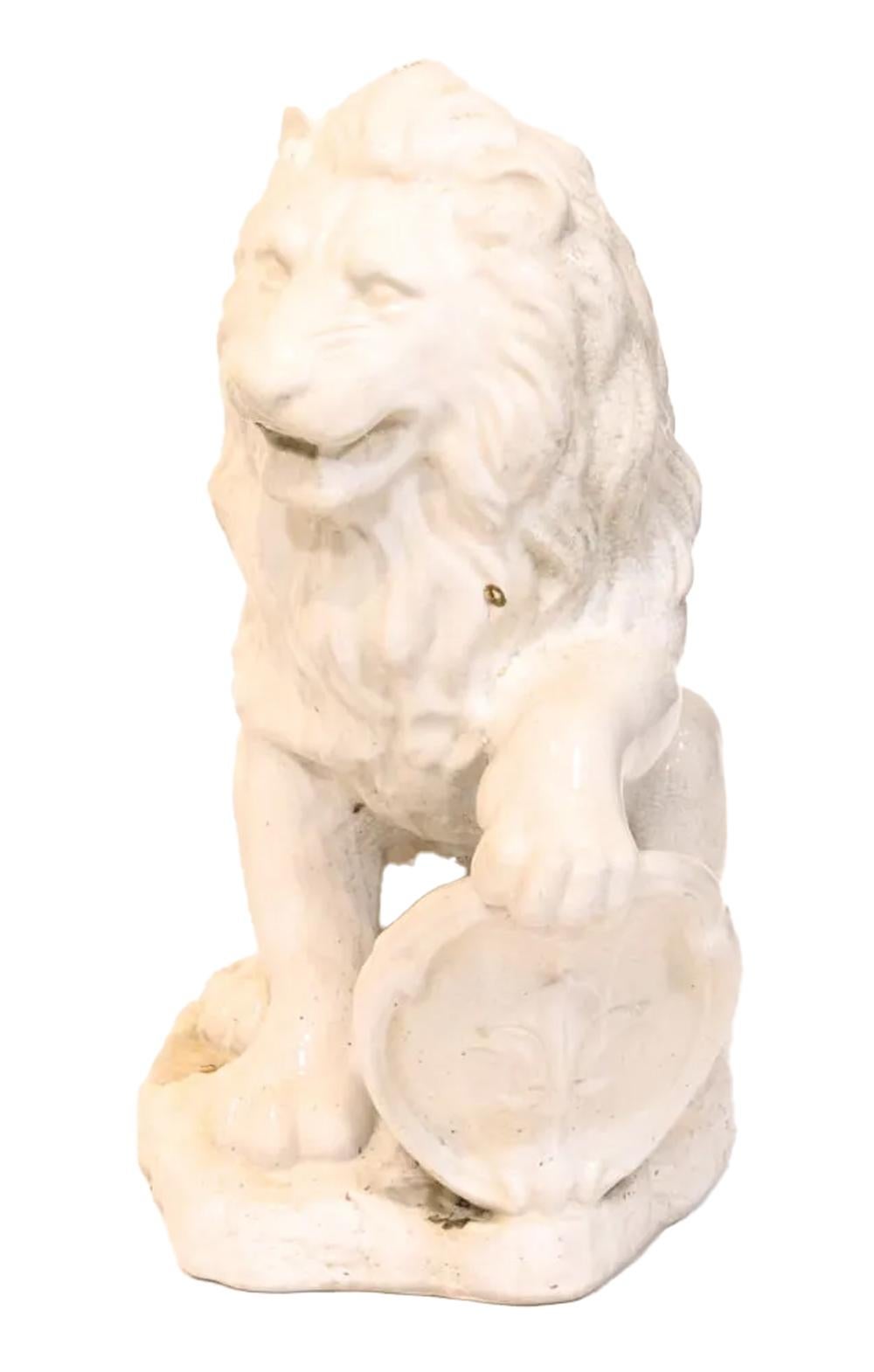 A pair of white glazed ceramic lions of imposing size. Each with his mouth slightly open and seated on a shaped plinth and in mirror image poses with opposing paws raised on shields with central fleur-de-lis designs. The white ceramic body glazed