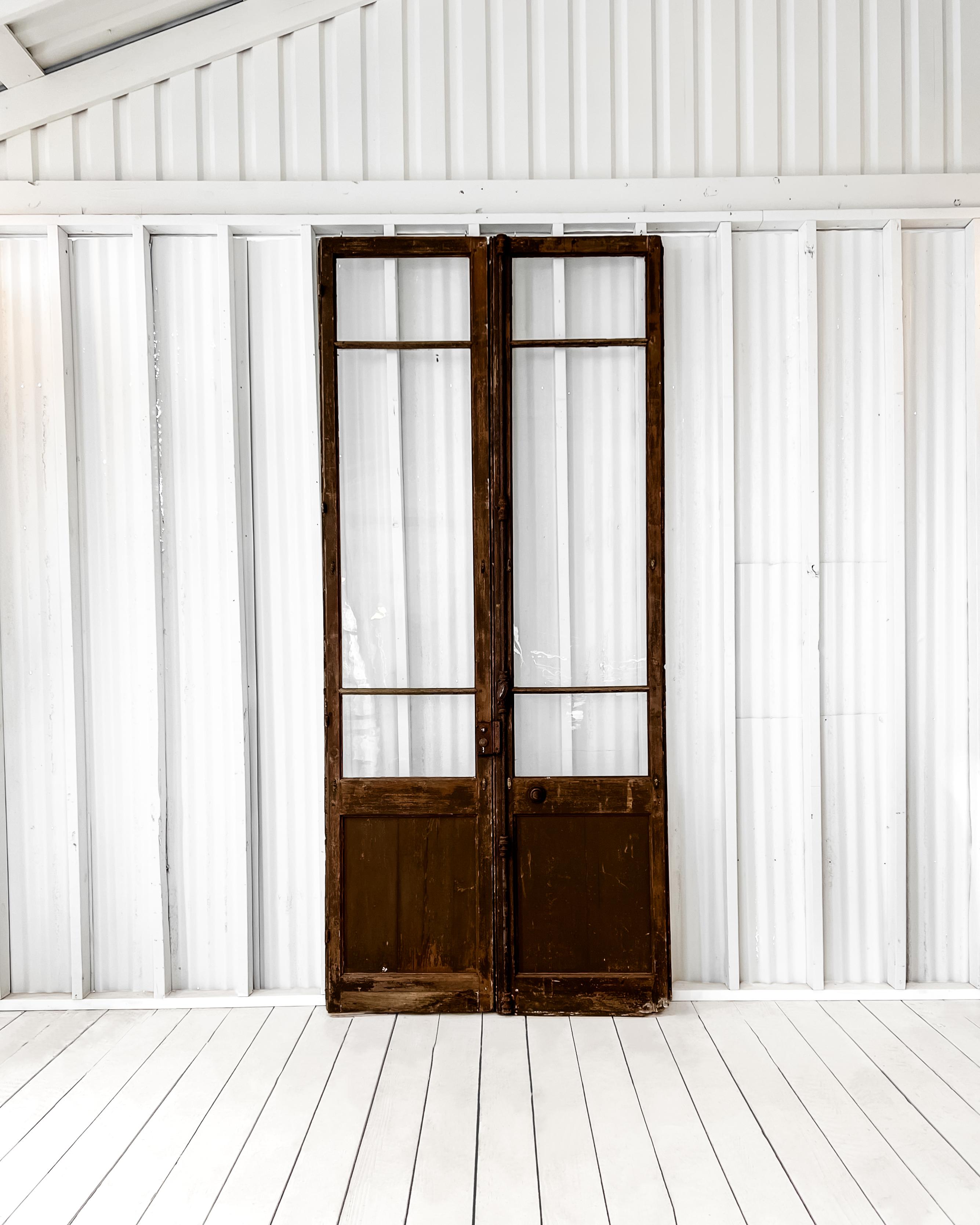 Found in France, dating to the late 18th century, from a prominent chateau, this pair of 3 lite panel doors retain their original glass, although one has suffered a crack. The original espresso paint has worn and weathered beautifully over time.