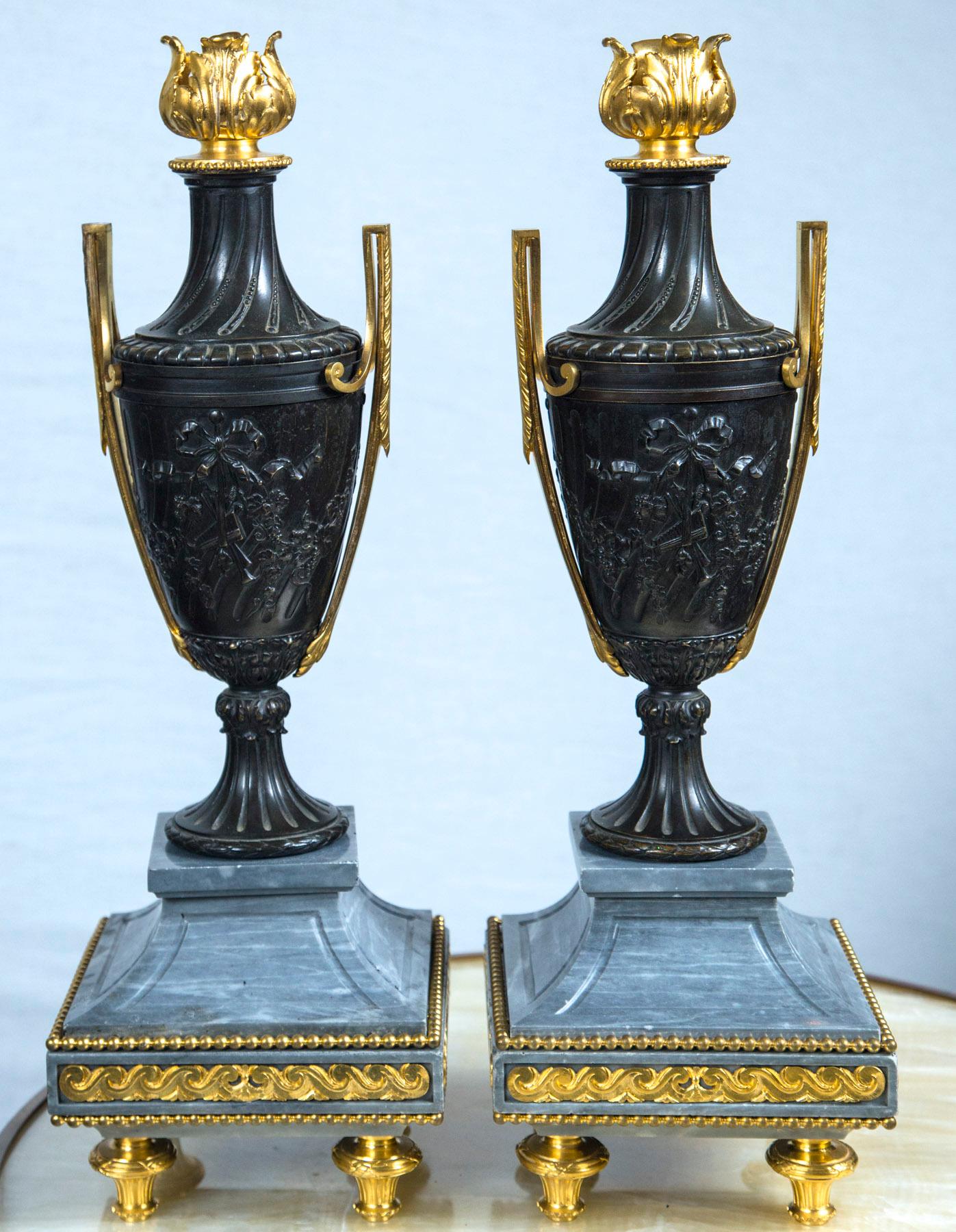 Raised on gilt bronze toupee feet. Gilt decoration on 3 sides of the grey marble bases Gilt bronze handles. Gilt bronze floral finial. The patinated bronze decorated in relief with bow topped trophies on each side. The bases measure 6.5 x 6.5. The