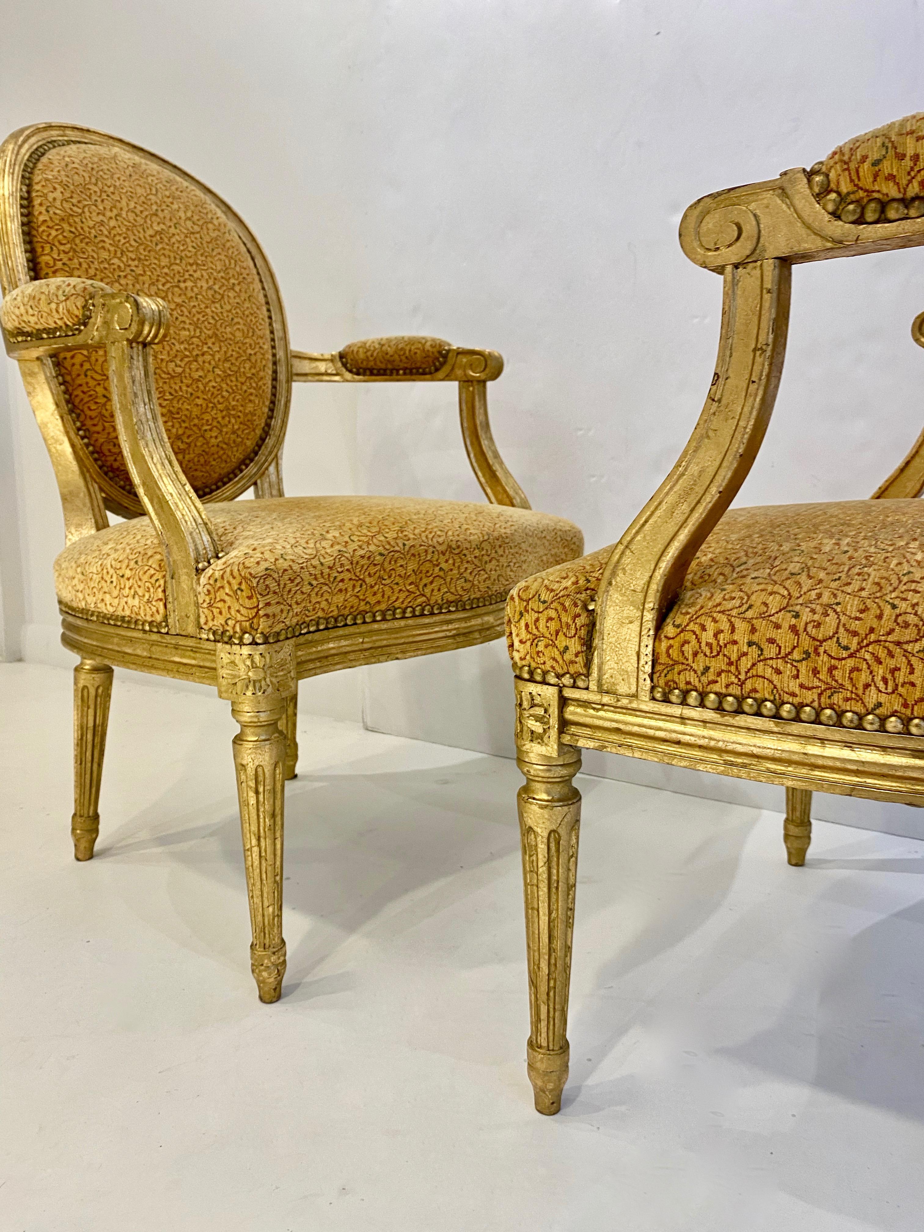 A beautiful pair of Louis XV style giltwood armchairs with fluted tapered legs and a nailhead detail. These chairs are covered in a pattered chenille fabric with rounded backs.