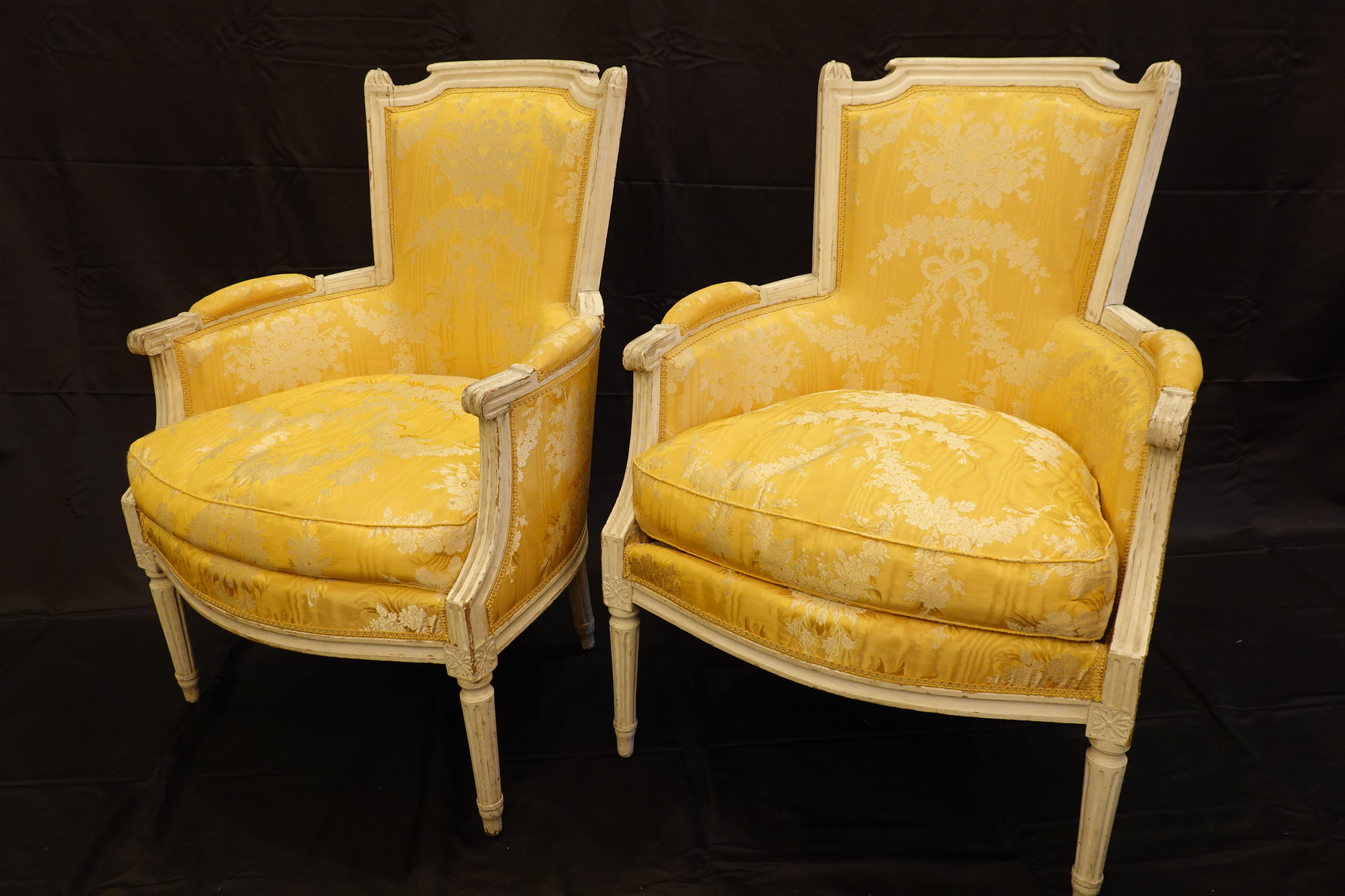 Pair of stunning French Louis XVI period bergères, upholstered in yellow silk lampas brocade fabric and gimp trim, with separate down-stuffed seat cushions (Circa 1790). The chair frames are white-painted, with 