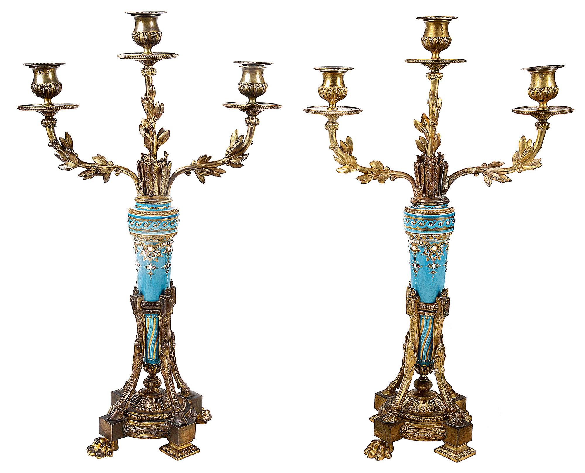 Pair of Louis XVI style candelabra, each with bold turquoise ground arrow sheaths with jewelled and gilded decoration, three branch sconces with foliate detail. Raised on triform bases with hoof and claw feet.
 