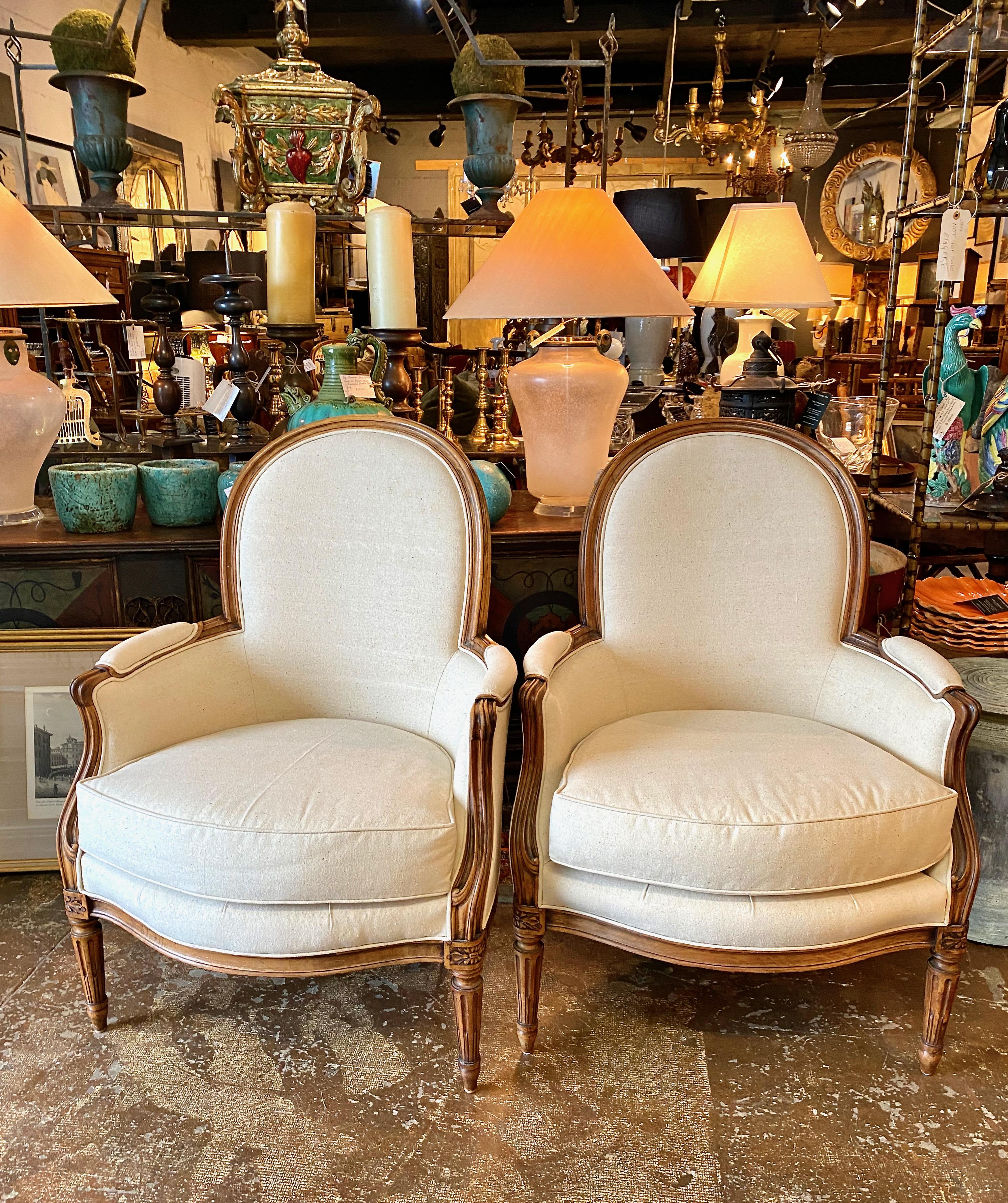 This is a classic pair of Louis XVI-style bergeres that date to the mid 19th century. The well-hand carved frames appear to retain their original surface in very good condition. The chairs are generously proportioned and are newly upholstered in a