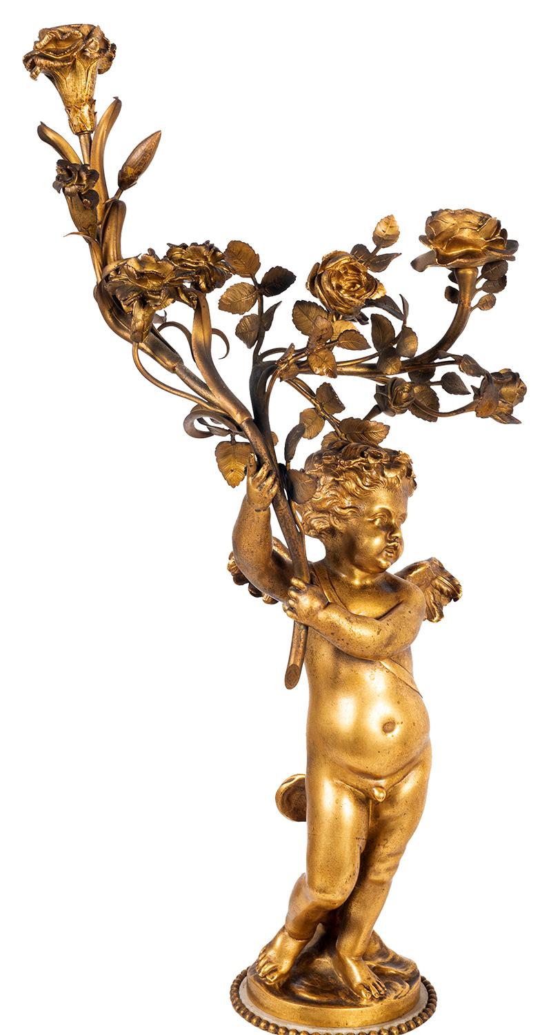 A good quality pair of 19th Century gilded ormolu and white marble Louis XVI style two branch candelabra, each having floral decoration, supported by cherubs, raised on circular pedestals, ormolu bands with scenes of various cherubs playing musical