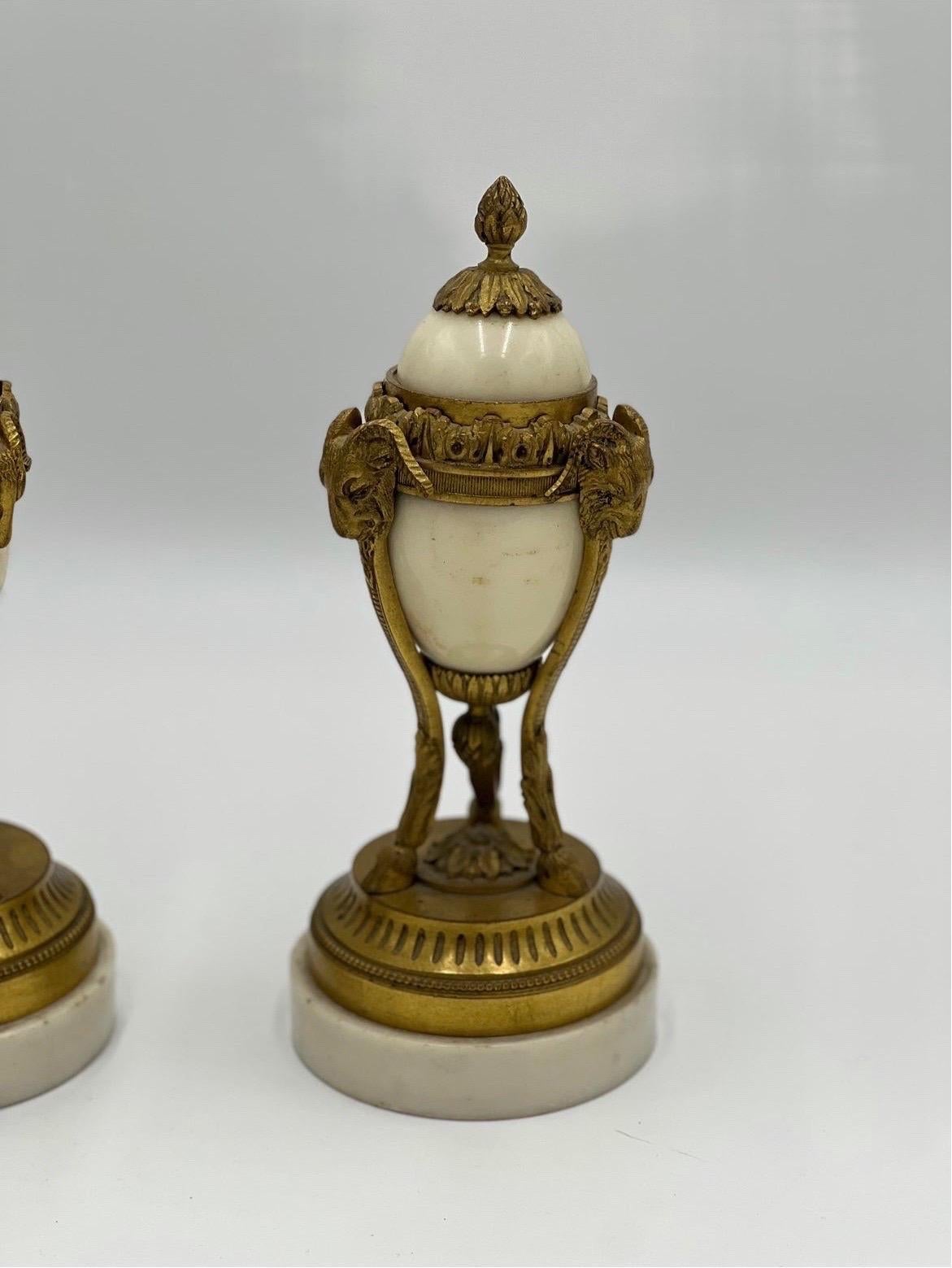A pair of 19th century Louis XVI style gilt bronze and white marble cassolettes. Each decorated with 3 ram’s heads supported by hoof feet, beaded accent and removable lids.