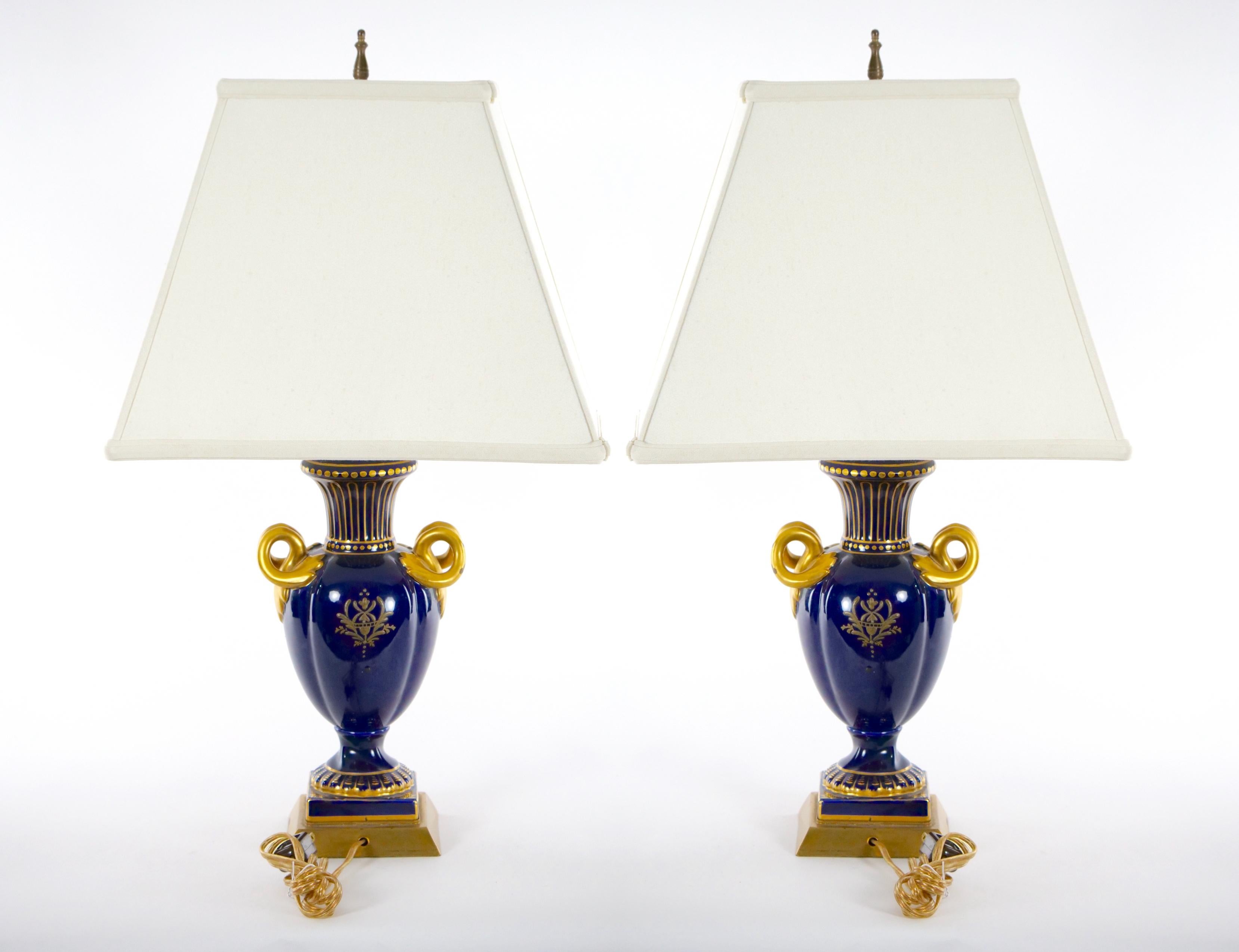 Early 20th century Louis XVI style French porcelain and hand gilt gold decorated urn shape vase pair table lamp. Each lamp features on one side a painted pastoral scenes decorated design. The reverse is a gilt gold painted with what appears to be a