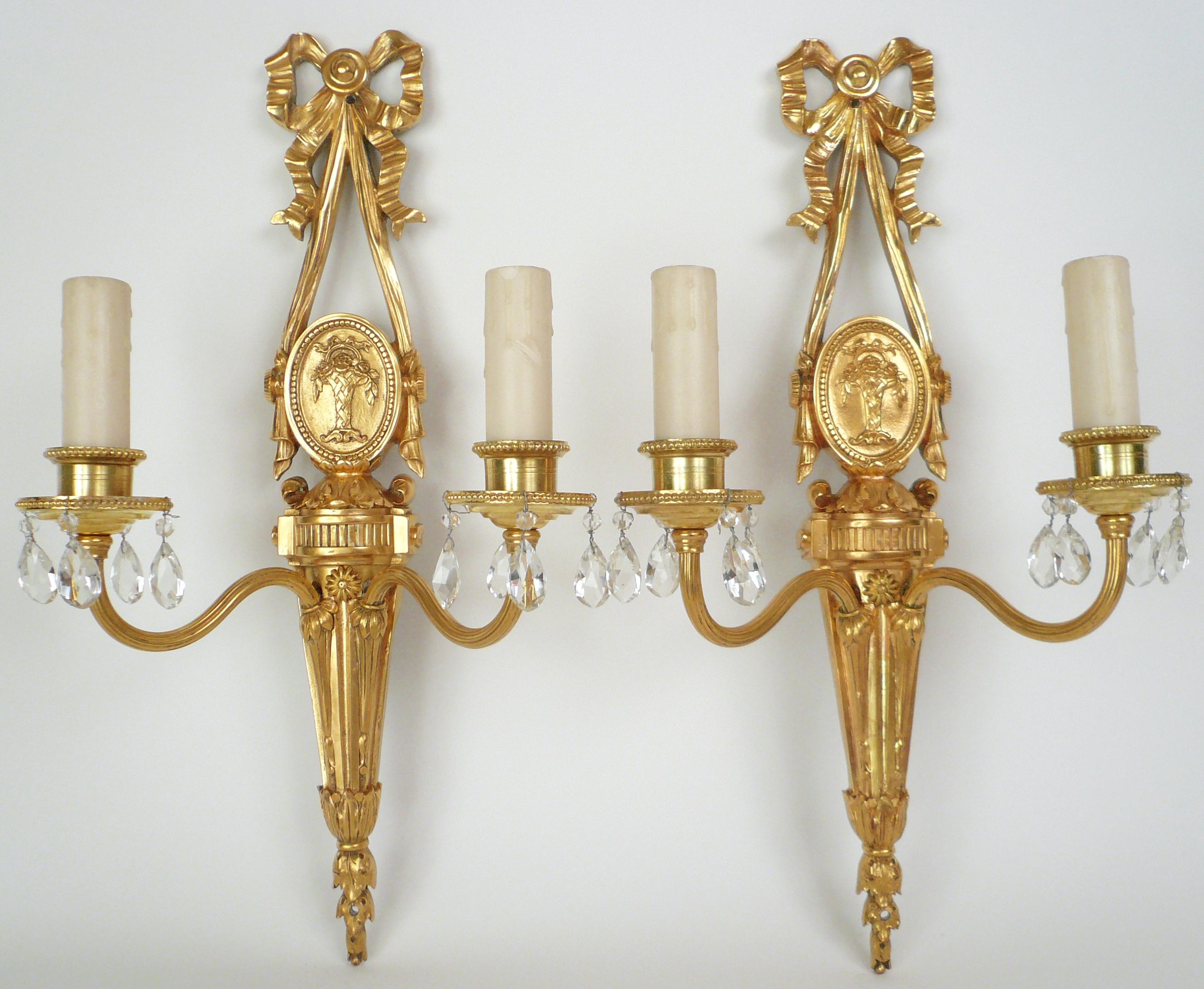 This pair of gilt bronze sconces feature Neo-Classical motifs including bowknots, acanthus leaves, and oval medallions featuring baskets of roses. They retain their original finish, and are signed Caldwell.