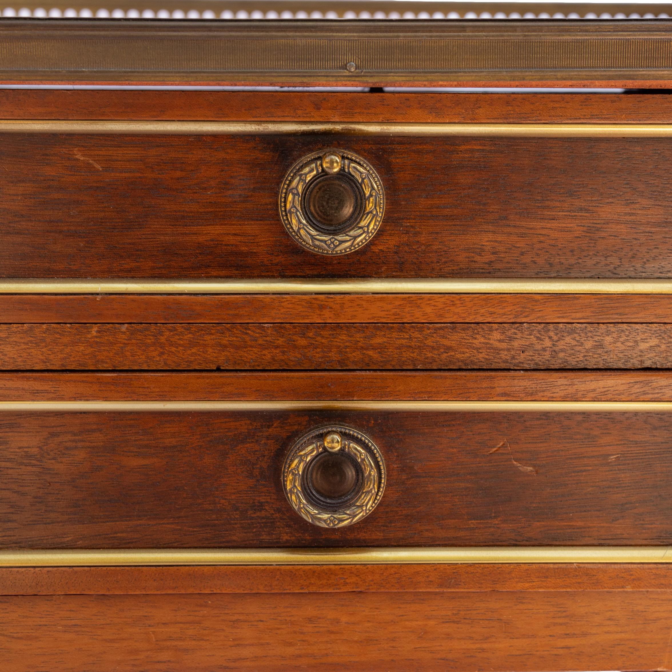 A Pair of Directoire-style mahogany two-drawer side tables, with bronze ormolu bands, and marble tops with filigreed gallery, on reeded legs terminating with gilt bronze sabots, French, ca. 1880.  The backs are finished. 