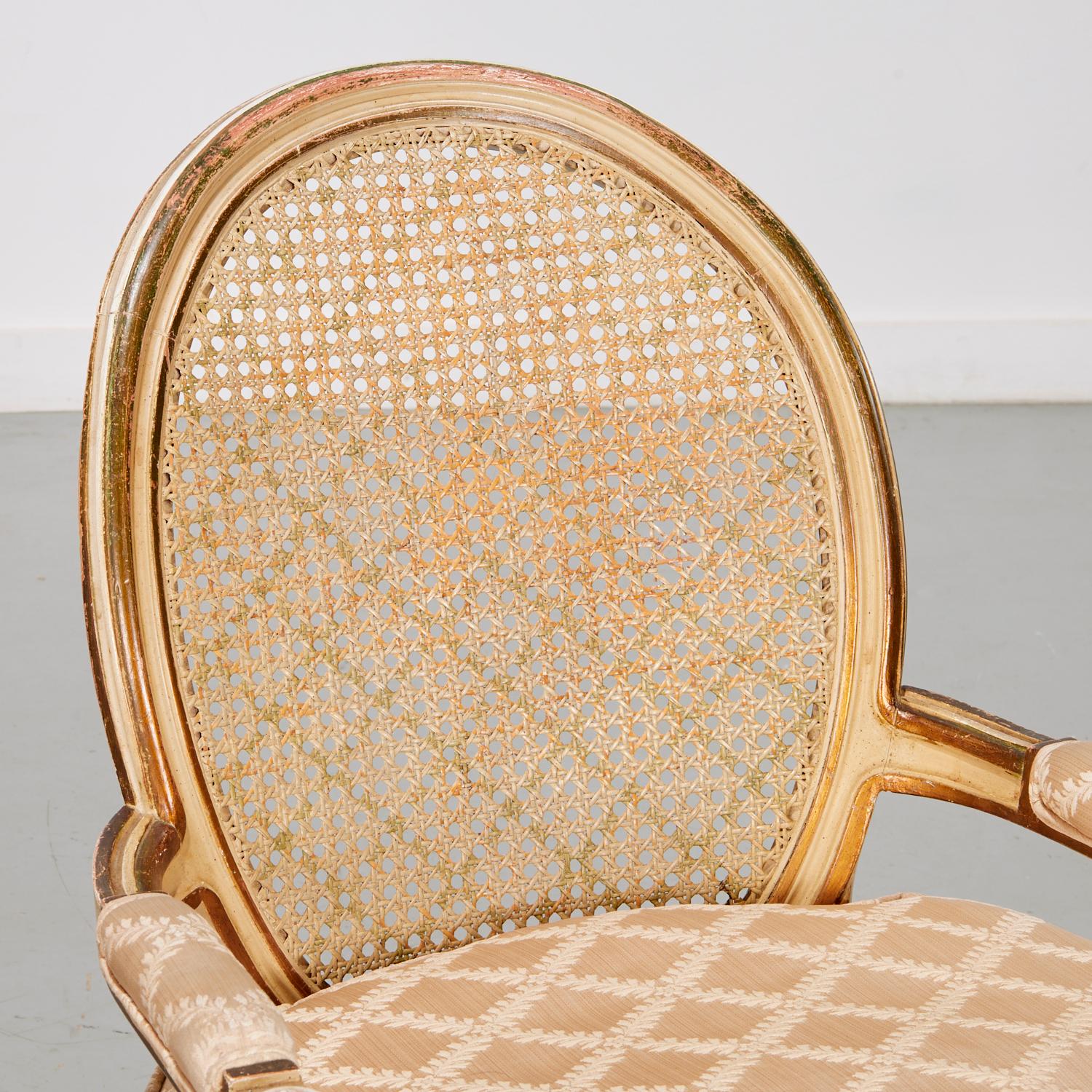 Au milieu du 20e siècle, une paire de fauteuils peints de style Louis XVI à dossier cannelé et sièges rembourrés sur des pieds cannelés effilés. Les chaises sont peintes à la main en crème avec des détails dorés. Le dossier canné et le tissu