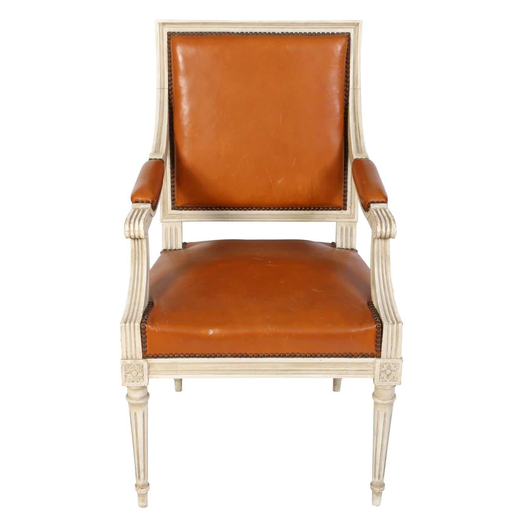 A pair of painted white and carved Louis XV style arm chairs with orange leather seats, backs and arm rests and nail head trim to square shaped backs.
