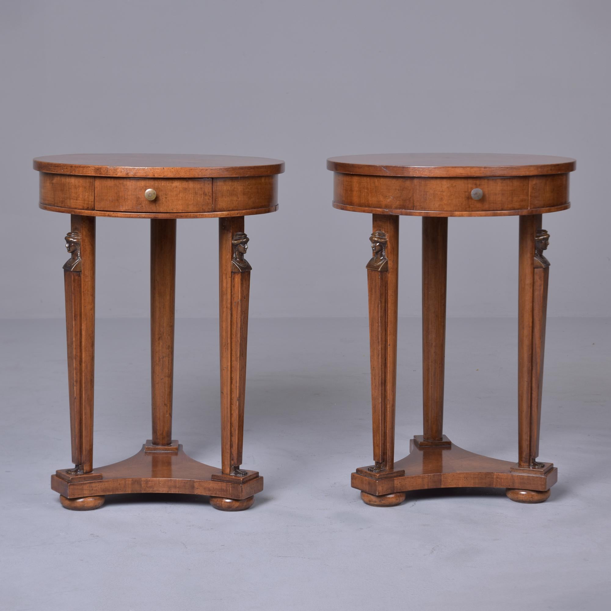 Found in France, this pair of Louis XVI style side tables date from approximately 1900. Each of these round tables has a decorative veneer pattern on top, small functional drawer and carved, classical busts at the top of the three legged base.
