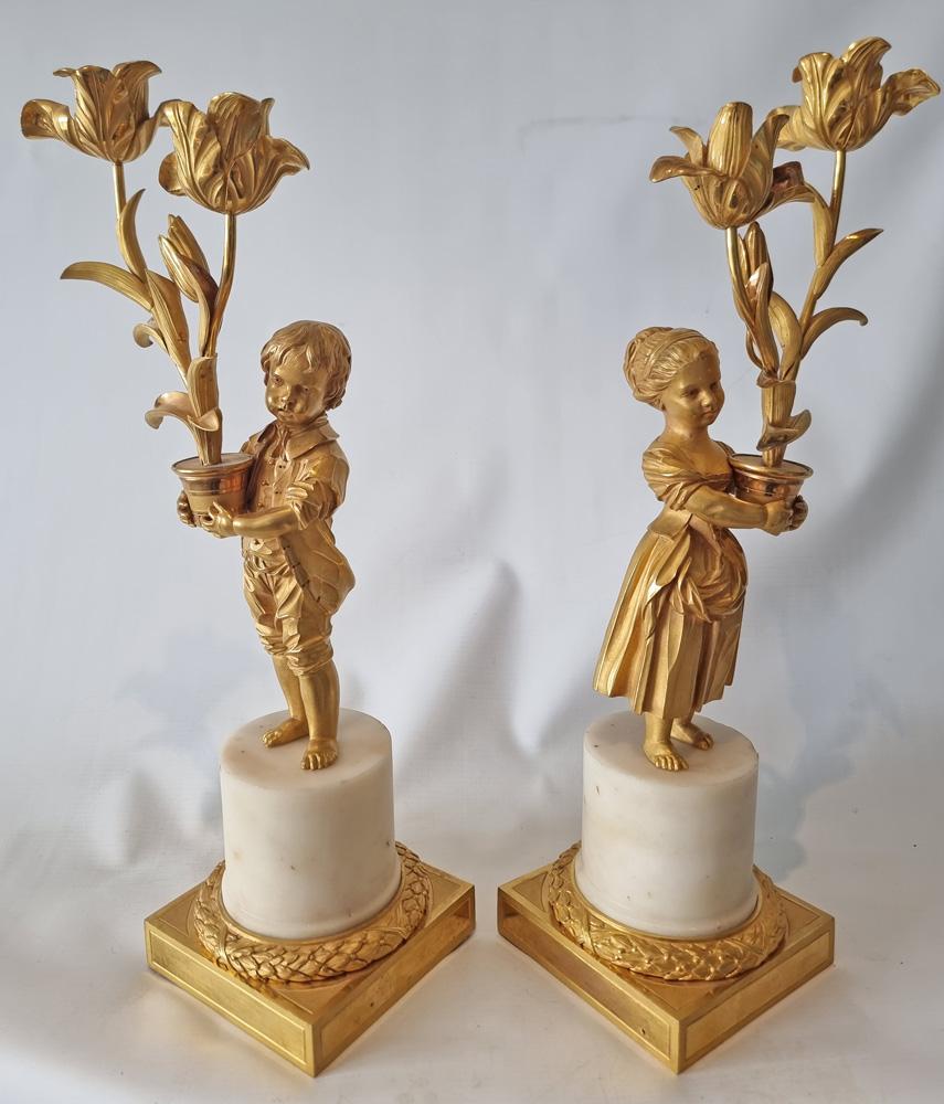 Superbe paire de candélabres de transition Louis XVI en bronze doré et marbre blanc. Elle repose sur une base carrée en bronze doré et un socle en marbre blanc. Chaque figure est magnifiquement sculptée et finie à la main par le Graveur après le
