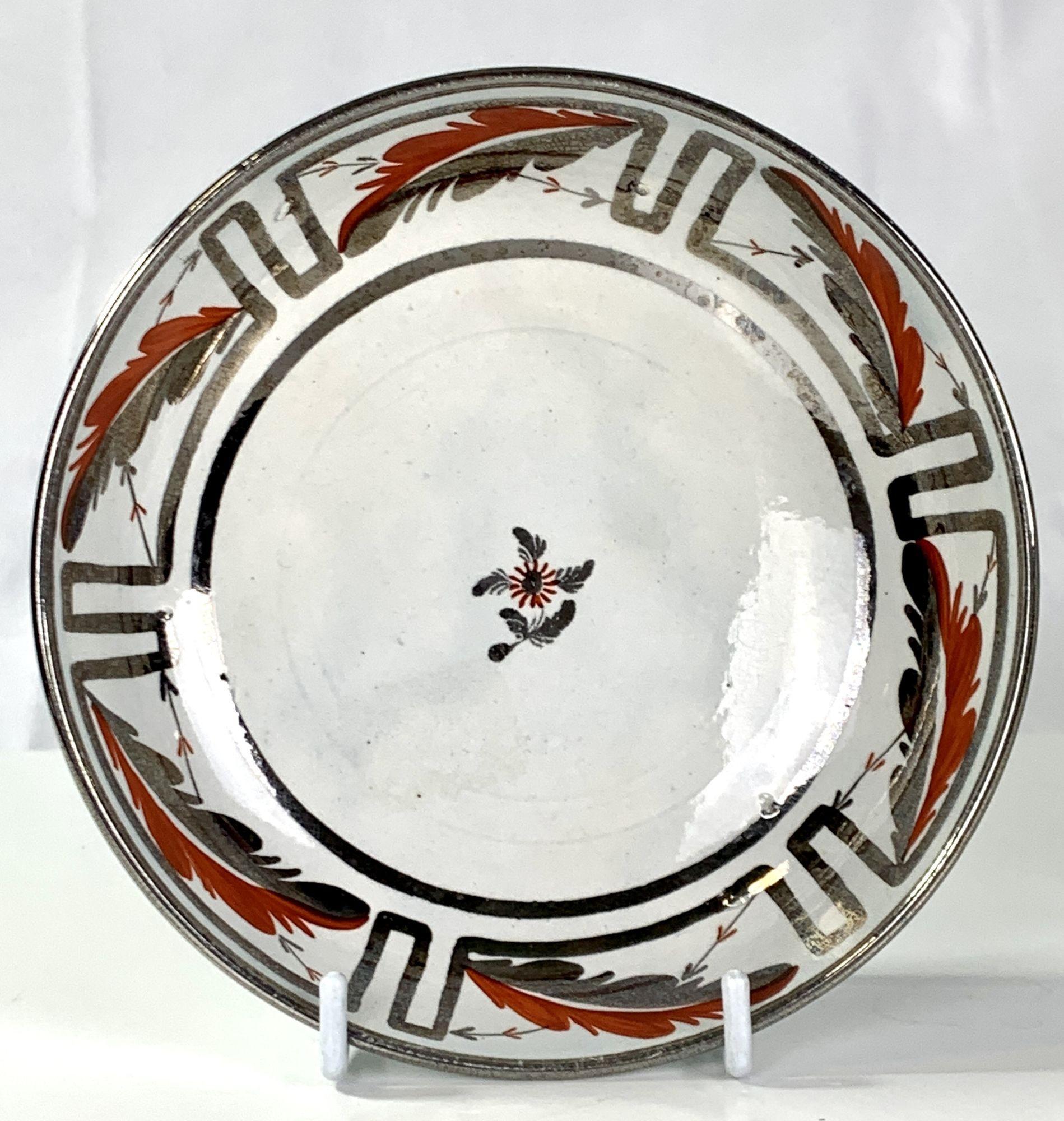 This pair of English silver Lustre cups and saucers have neoclassic decoration. 
 On the border, panels of silver lustre frame a single acanthus leaf painted half in lustre and half in red enamel.
The center of each saucer shows a simple red
