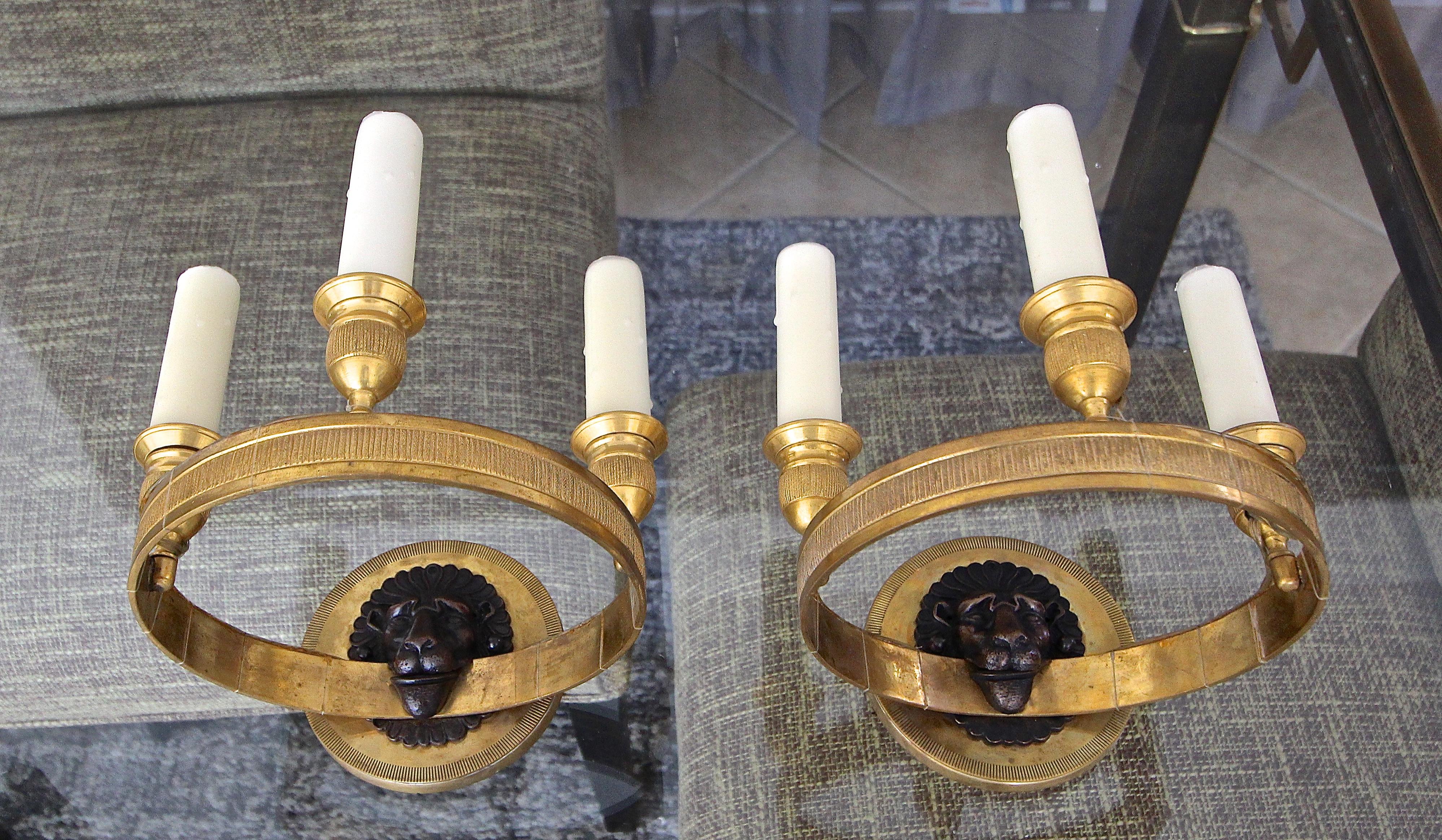 Pair of French brass (or bronze) Directoire style wall sconces with 3-light candleholders. Expert detailing throughout including lion face motif. Each of the 3 lights uses a candelabra size bulb. Back plate 4.5