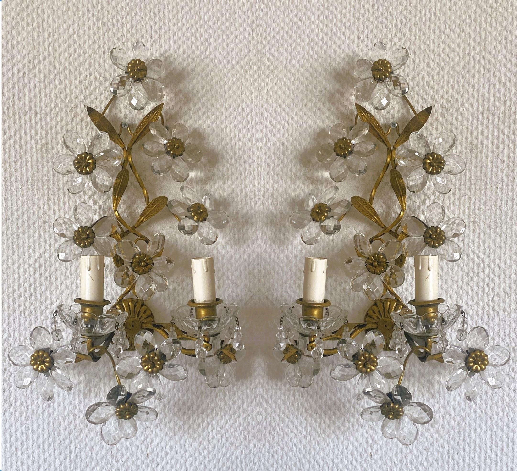Pair of Maison Bagès gilded wrought iron two-arm wall lights, France, 1920s. Wonderful art environment handcrafted in wrought iron and gilded, enriched with ten clear faceted crystal flowers (each sconce). In very good condition, no damages,