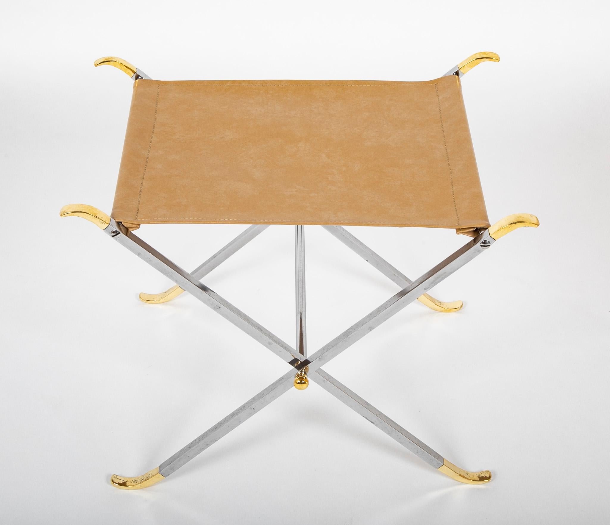 Quite elegant pair of polished steel and brass X-from stools with taupe leather seats. A very successful interpretation of the neoclassical style with clean and modern lines. Quintessential mid 20th century design. 
The stools fold for easy