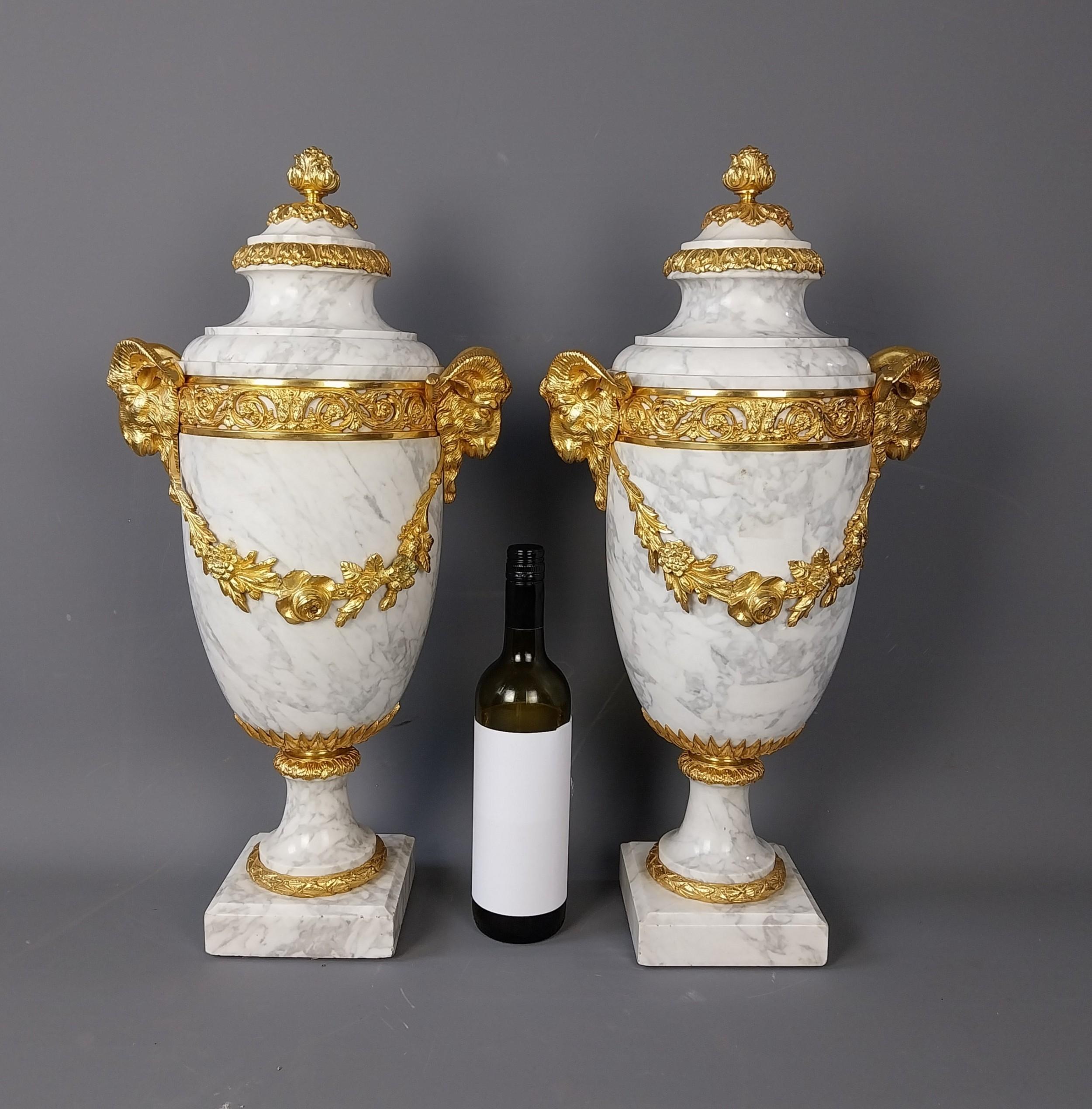 Una coppia di sostanziose cassolette del XIX secolo realizzate in pregiato marmo bianco di Carrara, impreziosite da intricate montature in bronzo dorato (ormolu) fuse a forma di teste di Rams che reggono ciascuna una ghirlanda floreale Queste