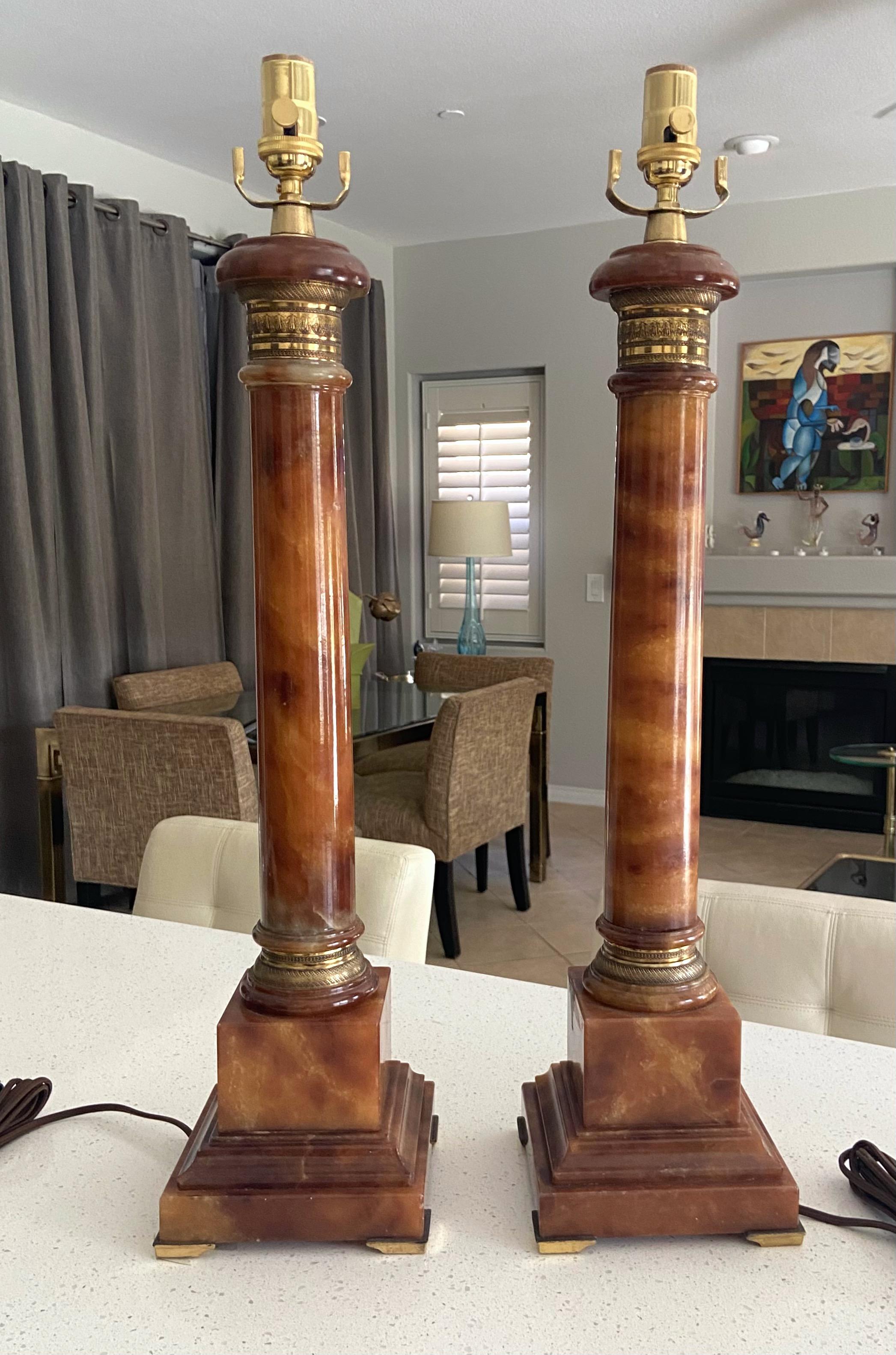 Pair of large hand carved neoclassic style column form alabaster lamps with brass mounted fittings. The color of the stone is rich amber with lots of color variation and veining. Manufactured by renowned lighting company Marbro (label was on the