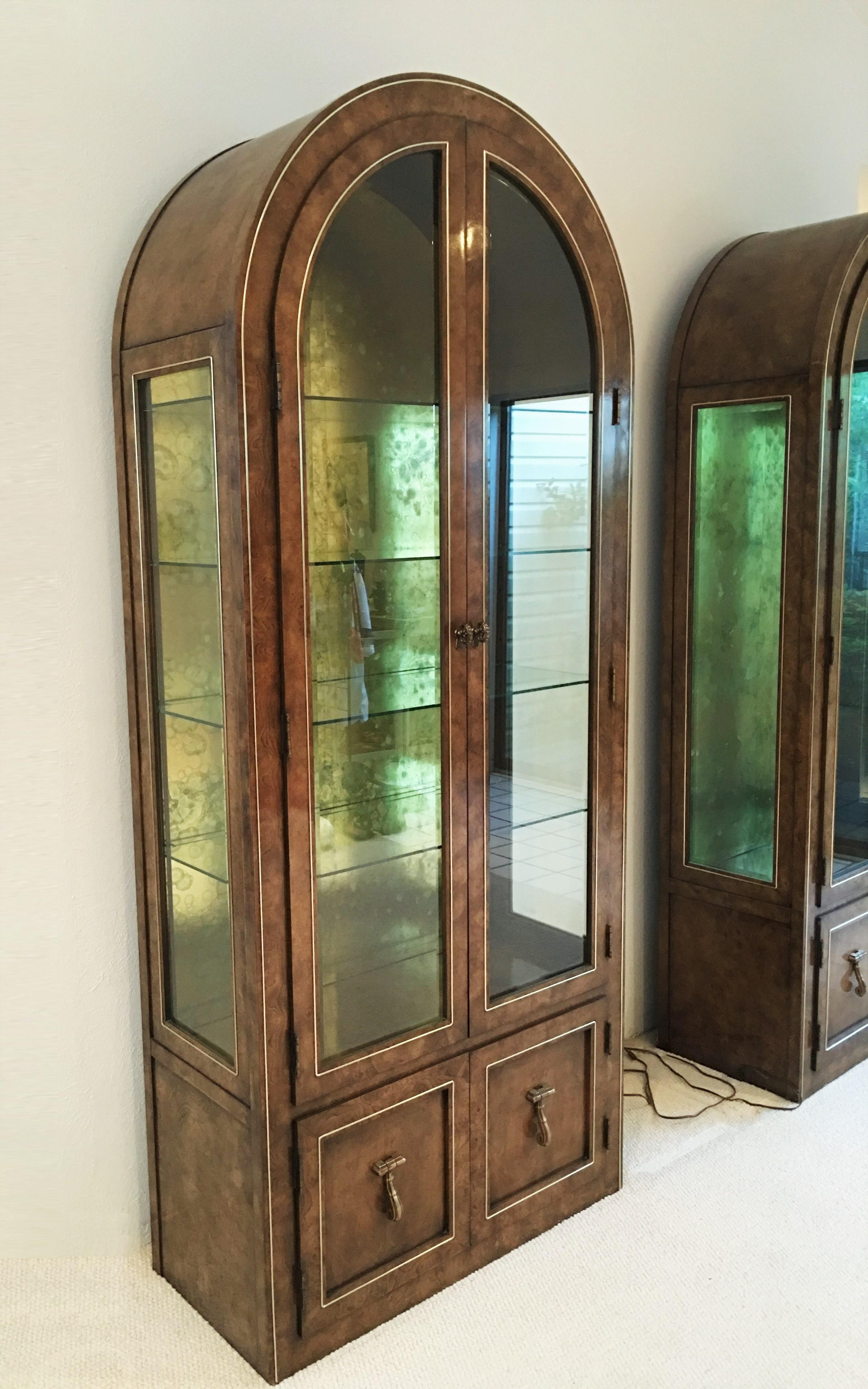 Eye-catching burled Amboyna wood and brass vitrine cabinets by William Doezema for Mastercraft. Set includes two free standing vitrines; large round-top burl wood cabinets each with four interior glass shelves, Featuring beveled front and side glass