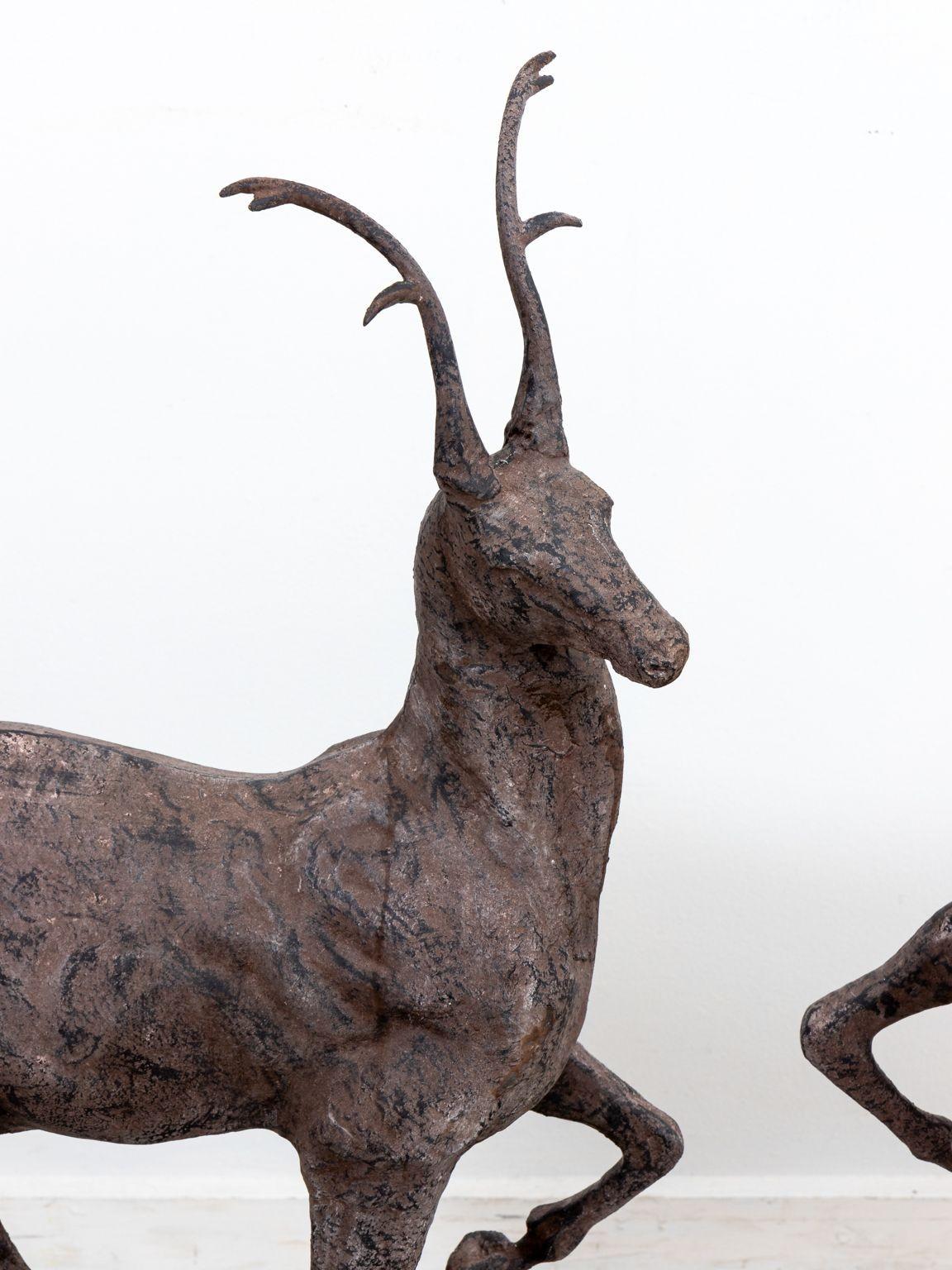 A pair of garden ornaments in the shape of deer or stags on globes. The deer are made of metal and are mirror images of one another. One front leg is elegantly lifted. Beautifully detailed antlers rise from the deer's heads. These are late 20th