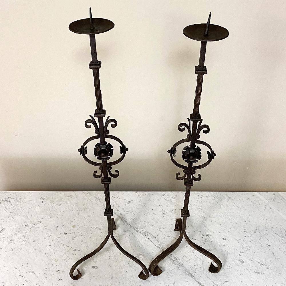 Pair of mid-19th century wrought iron torcheres ~ candlesticks were fashioned from red-hot iron by a talented blacksmith, and feature a nice height with twisted shaft and tripod base for stability even on slightly uneven surfaces. At the middle