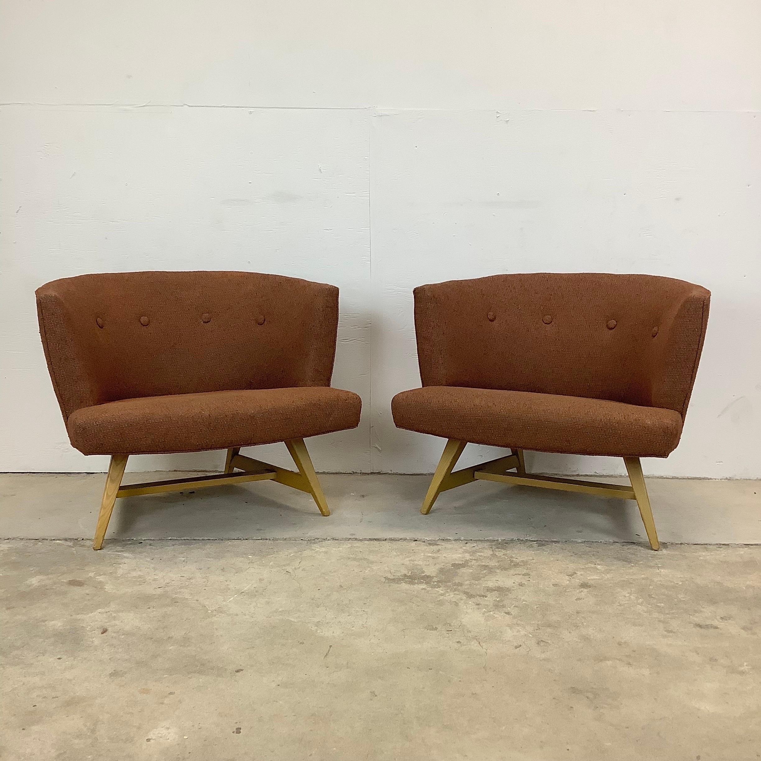 This impressive pair of matching Mid-Century Modern lounge chairs feature rounded barrel like seat backs with vintage brown upholstery and vintage wood frames. The comfortable proportions of this matching pair make them excellent accent chairs for
