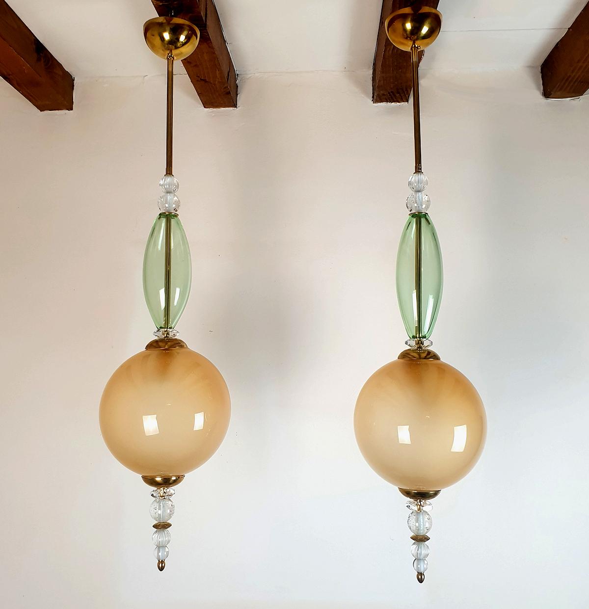 Pair of tall Mid-Century Modern pendant chandeliers, Murano glass & brass, attributed to Cenedese, Italy 1980s.
The vintage pair of pendants is made of a translucent beige globe nesting the light, clear light green and crystal cut elements, on a