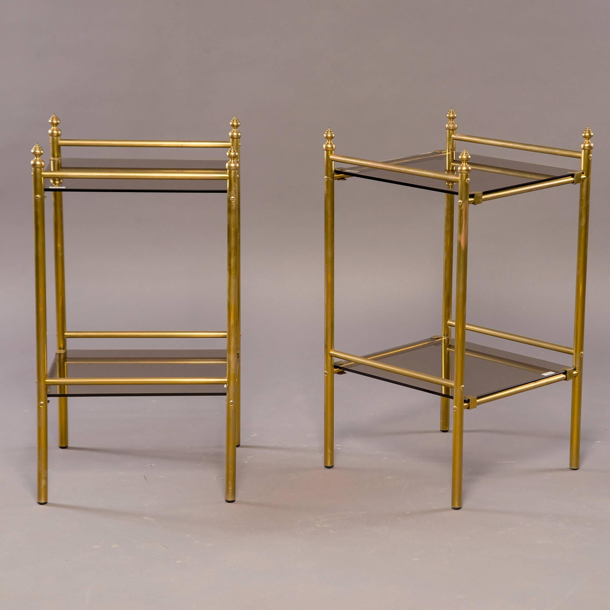 Pair of brass two-tier side tables have smoked glass shelves and tops and decorative finials, circa 1960s. Unknown maker. Found in France. Sold and priced as a pair.