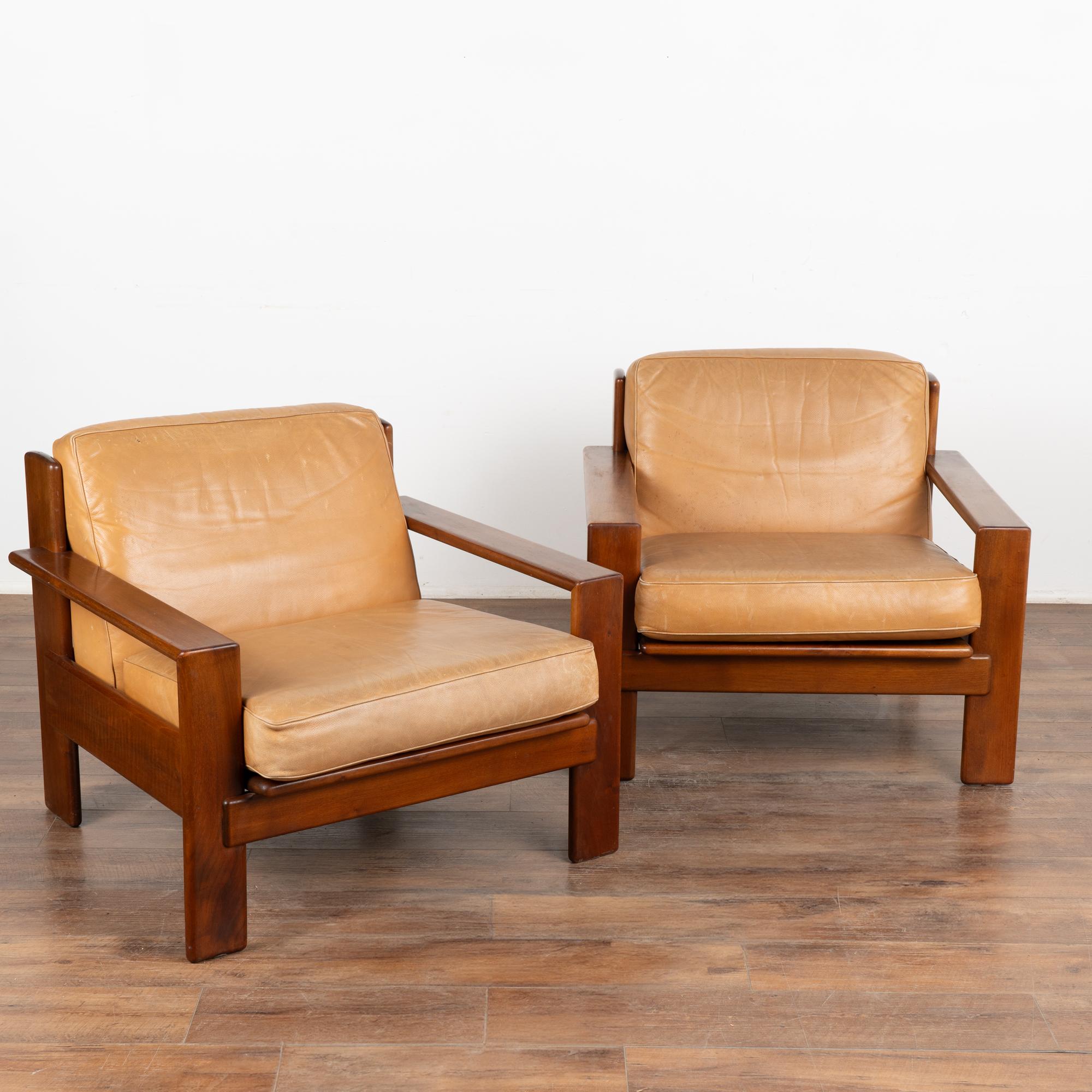This pair of arm chairs show off the clean lines of mid-century craftsmanship and style. 
In good used condition, the original camel leather shows typical signs of age-related wear such as scuffs, scratches, stains, impressions to leather and minor