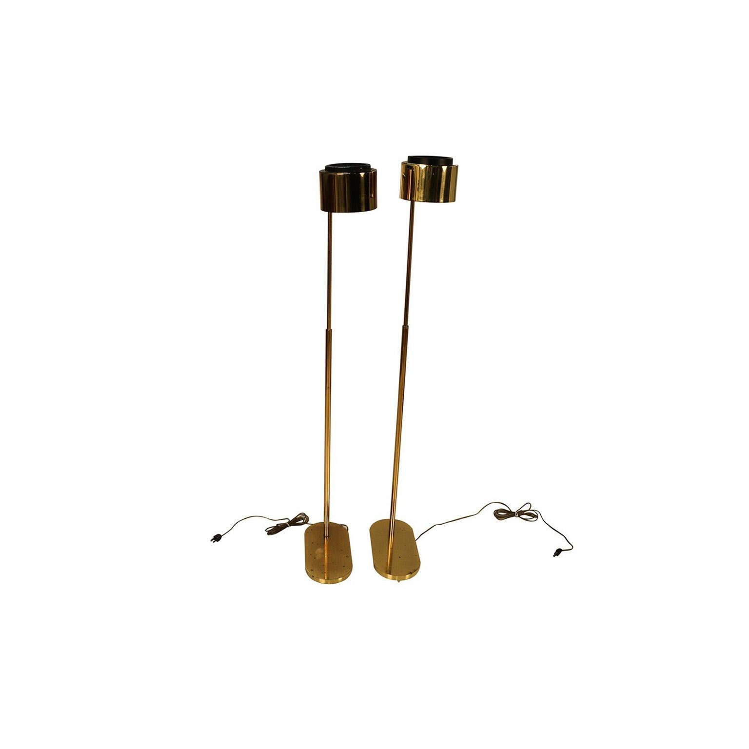 Magnificent pair of brass adjustable pharmacy floor lamps designed by Jon Norman for Casella Lighting. Each is impeccably constructed of brass. The heavy oval base supports an adjustable neck that’s finished with a cylindrical brass shade and black
