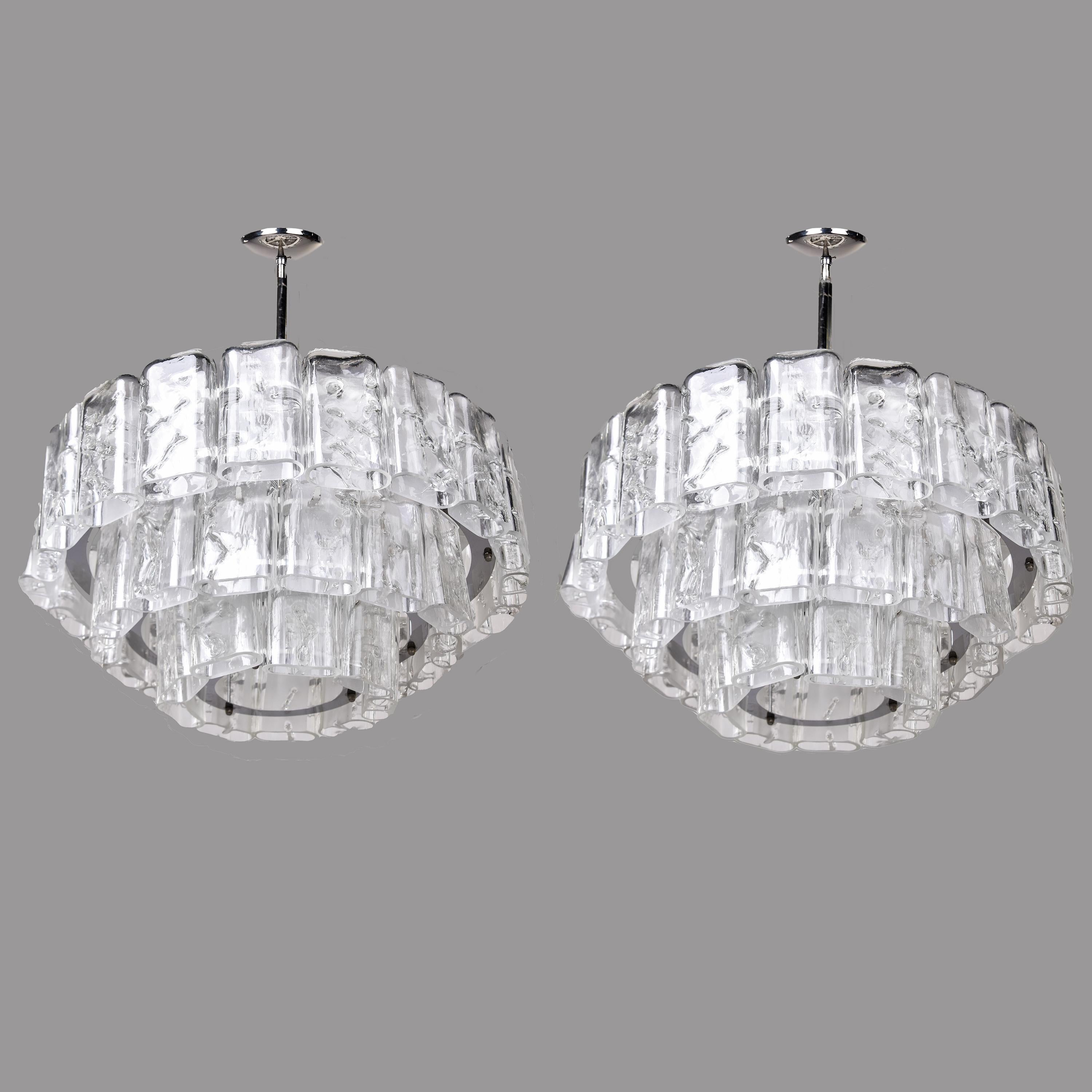 This pair of three tier modernist chandeliers by German maker Doria dates from the 1960s. Chandliers have metal frames with three graduated tiers of clear, oblong shaped glass pendants that have an icy appearance and polished edges. Each fixture has