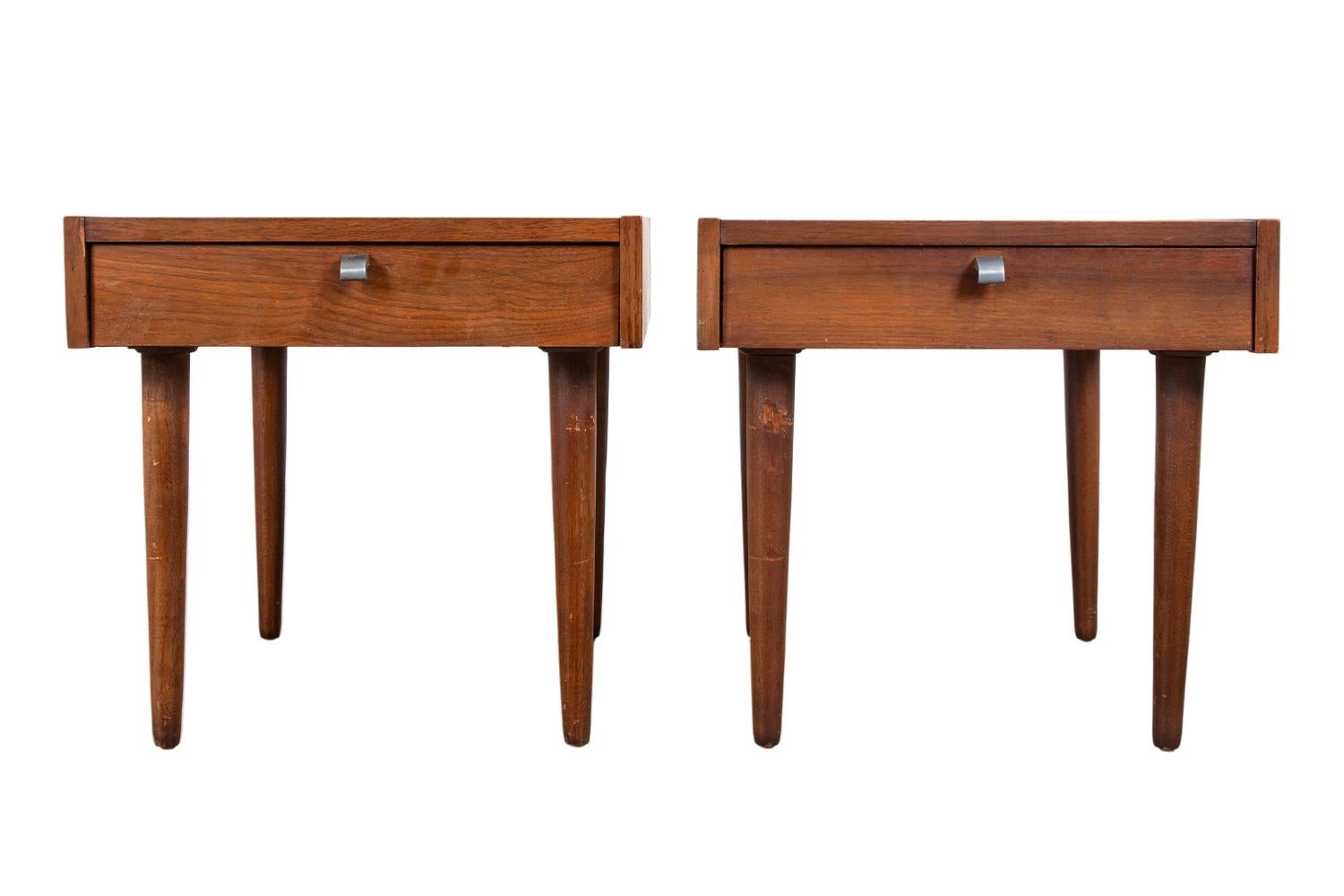 Striking pair of mid-century modern walnut nightstands or end tables by American of Martinsville, circa 1970’s, one of the most esteemed furniture producers of the Mid-century era. Each end table features a minimalist design with one spacious,