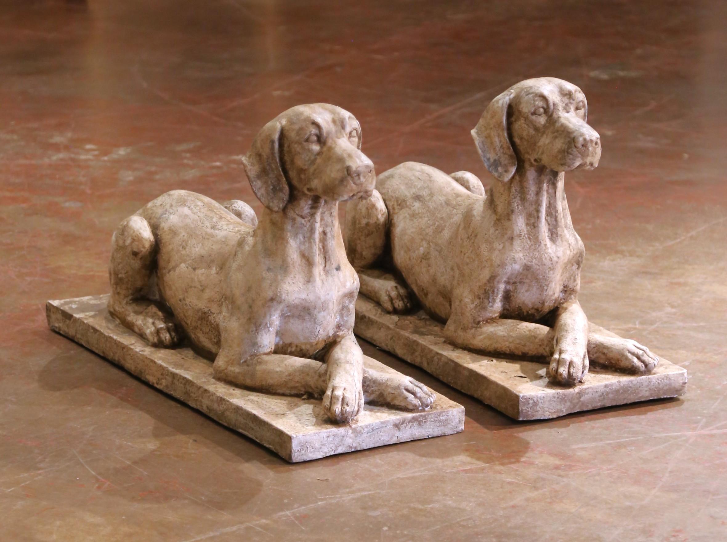 Bringen Sie zeitlosen Charme in Ihren Außenbereich mit diesem Paar Steinskulpturen aus der Mitte des Jahrhunderts, hergestellt um 1960. Jeder Hund ist in einer würdevollen, liegenden Pose dargestellt, mit gekreuzten Vorderpfoten und aufmerksam