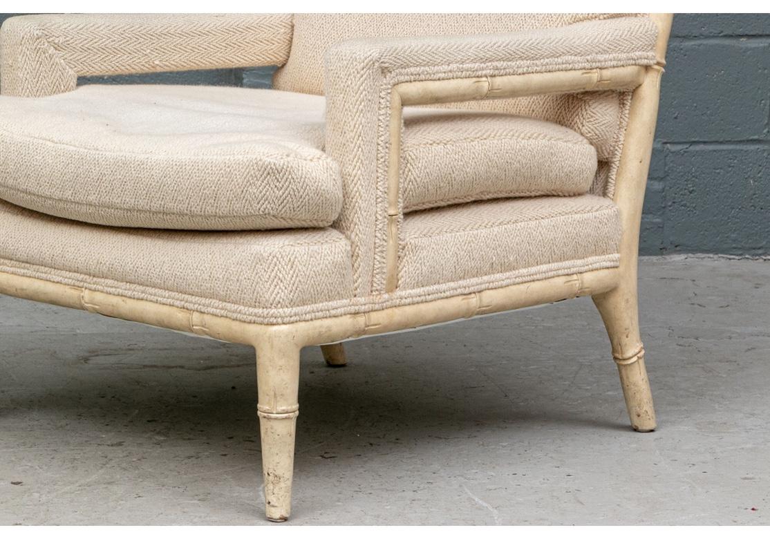 Finely constructed in faux bamboo carved wood in off-white pit in an antiqued finish. With sloping backs and raised on curved tapering cylindrical front legs and splayed back legs. Upholstered back, sides and seat cushions in a textured herringbone