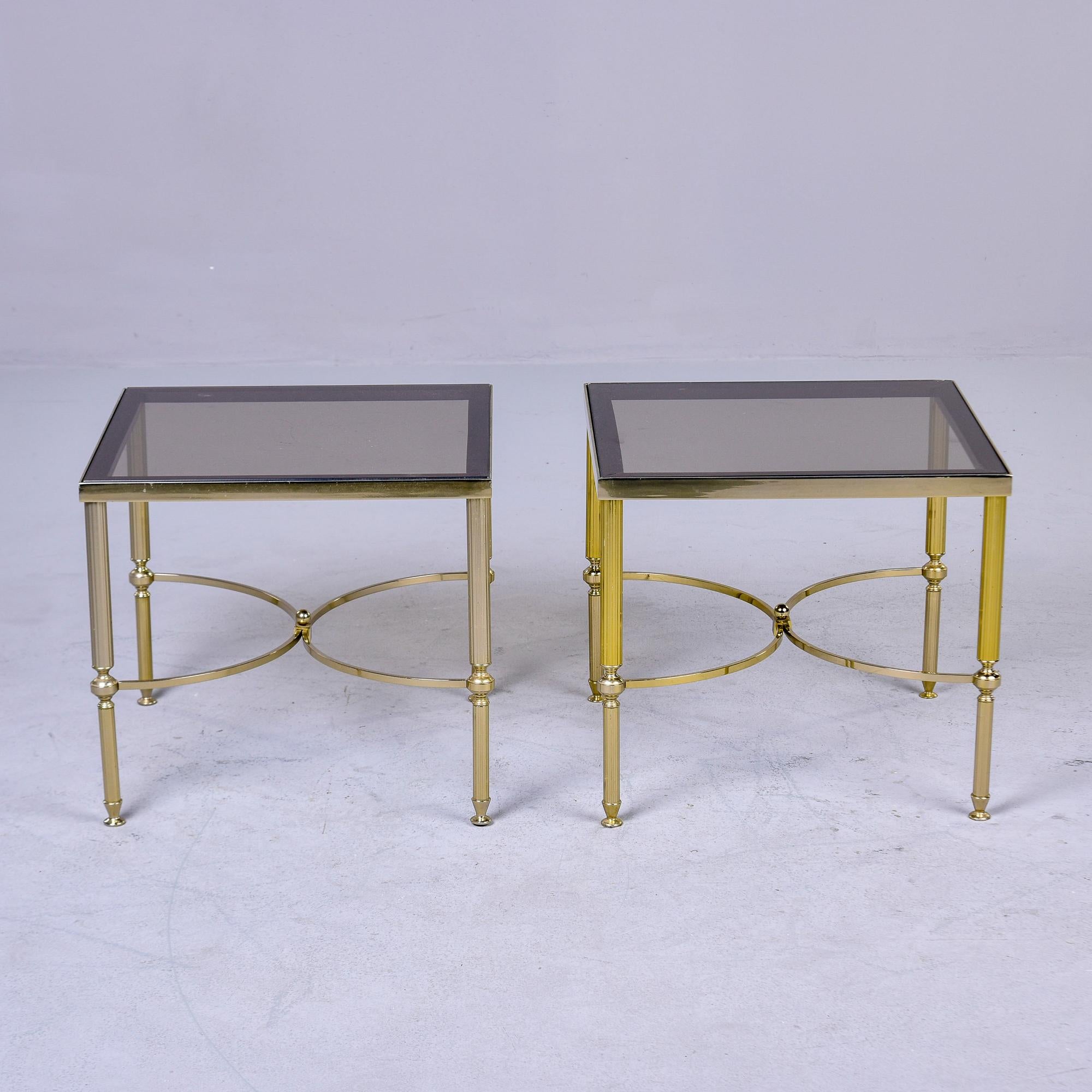 Found in France, this pair of side tables date from the 1960s.  Brass legs are reeded with little feet and decorative, curved stretchers. Inset table tops are light smoke colored glass tops. Sold and priced as a pair. Unknown maker. 