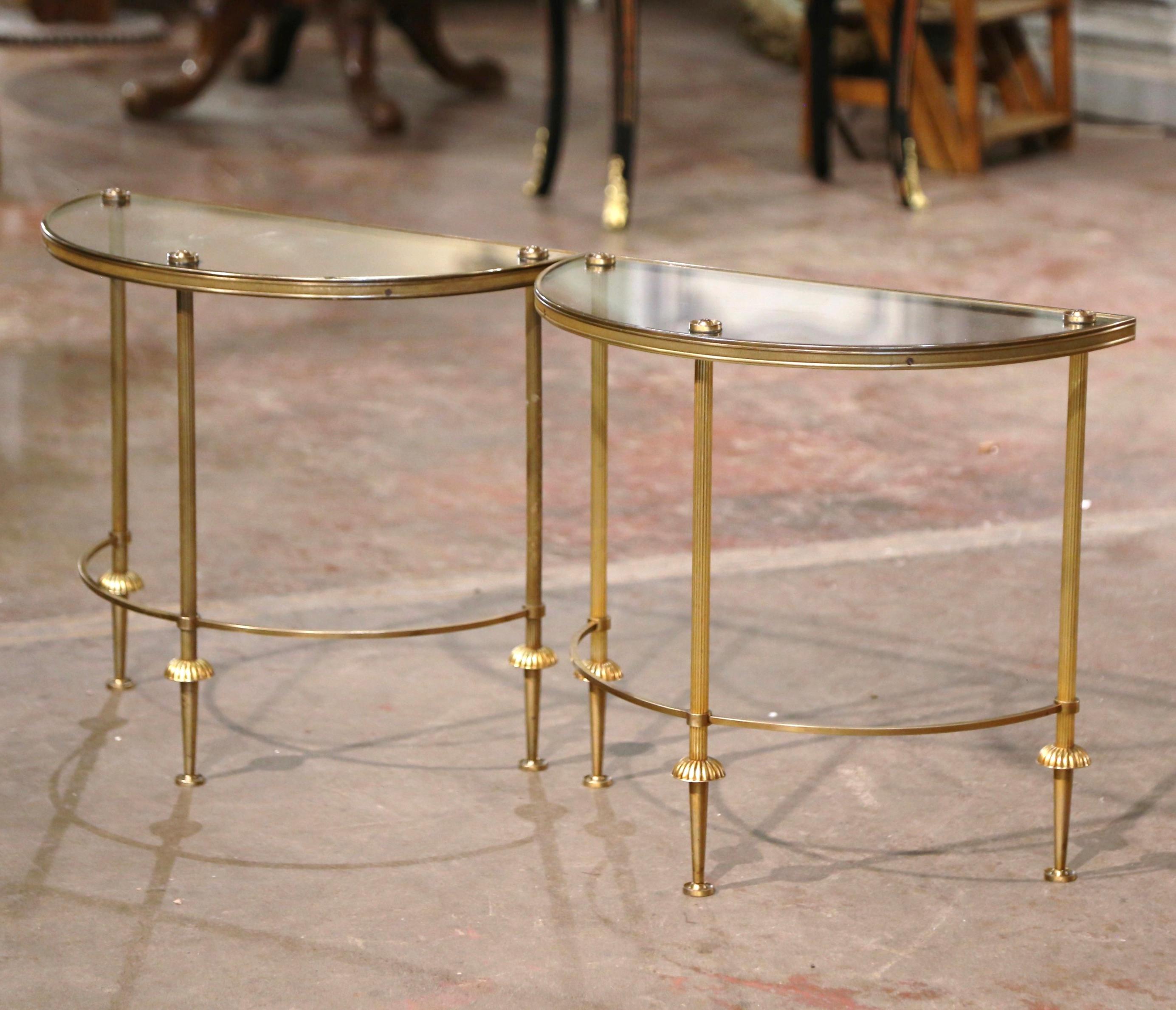 These vintage side tables attributed to Maison Baguès, were created in Paris circa 1950. Built of brass and shaped as half moon, each petite table stands on three fluted legs ending with tapered feet, over a bottom curved stretcher. Each surface is