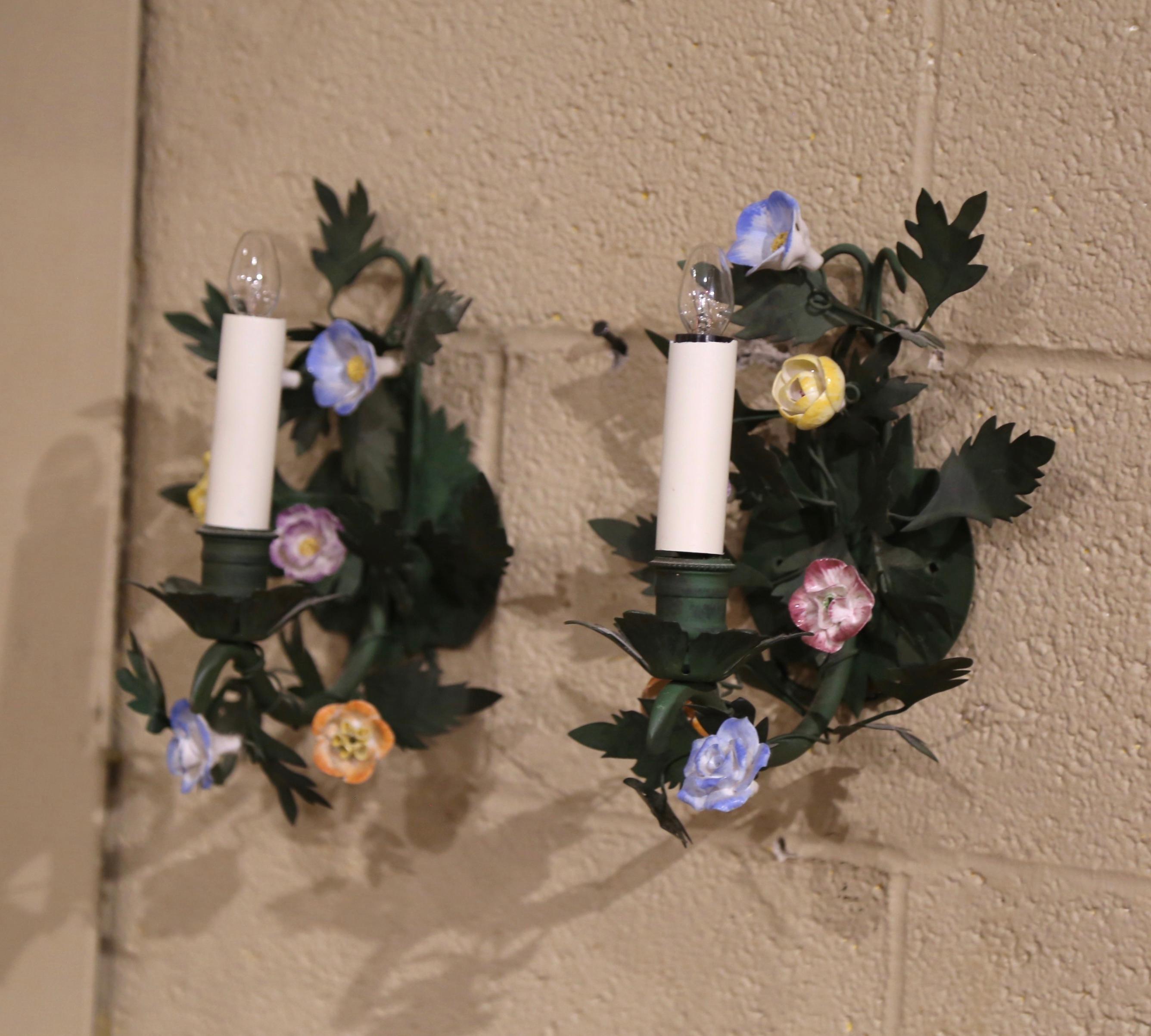 Decorate a powder room with this elegant and feminine pair of light fixtures. Crafted in France circa 1900, the petite single-arm antique sconces are decorated with orange and purple porcelain flowers and embellished with green leaves. The sconces