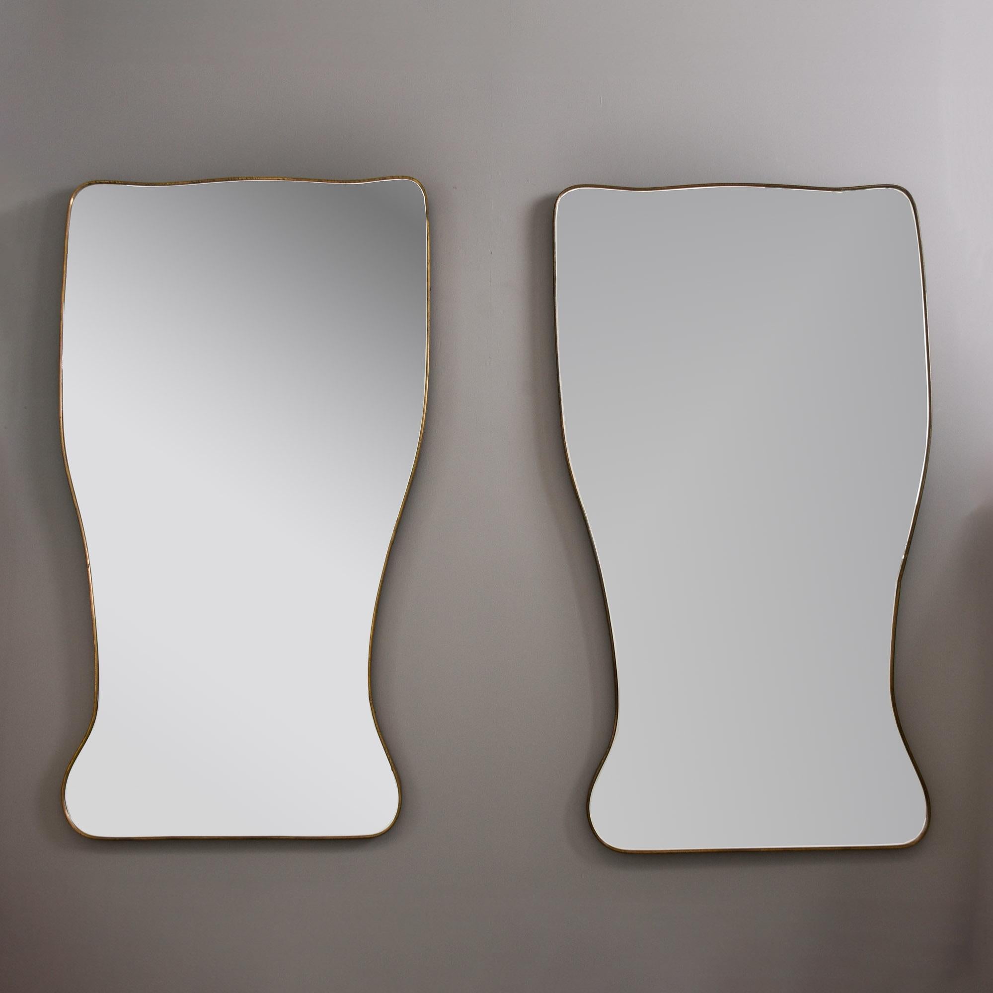 Found in Italy, this pair of mirrors date from the 1950s. Each mirror is 63” tall and has a slender brass frame and unusual, curvy rectangular form.  Wooden backs with hanging hardware - these could be hung with the narrower shape on top if you