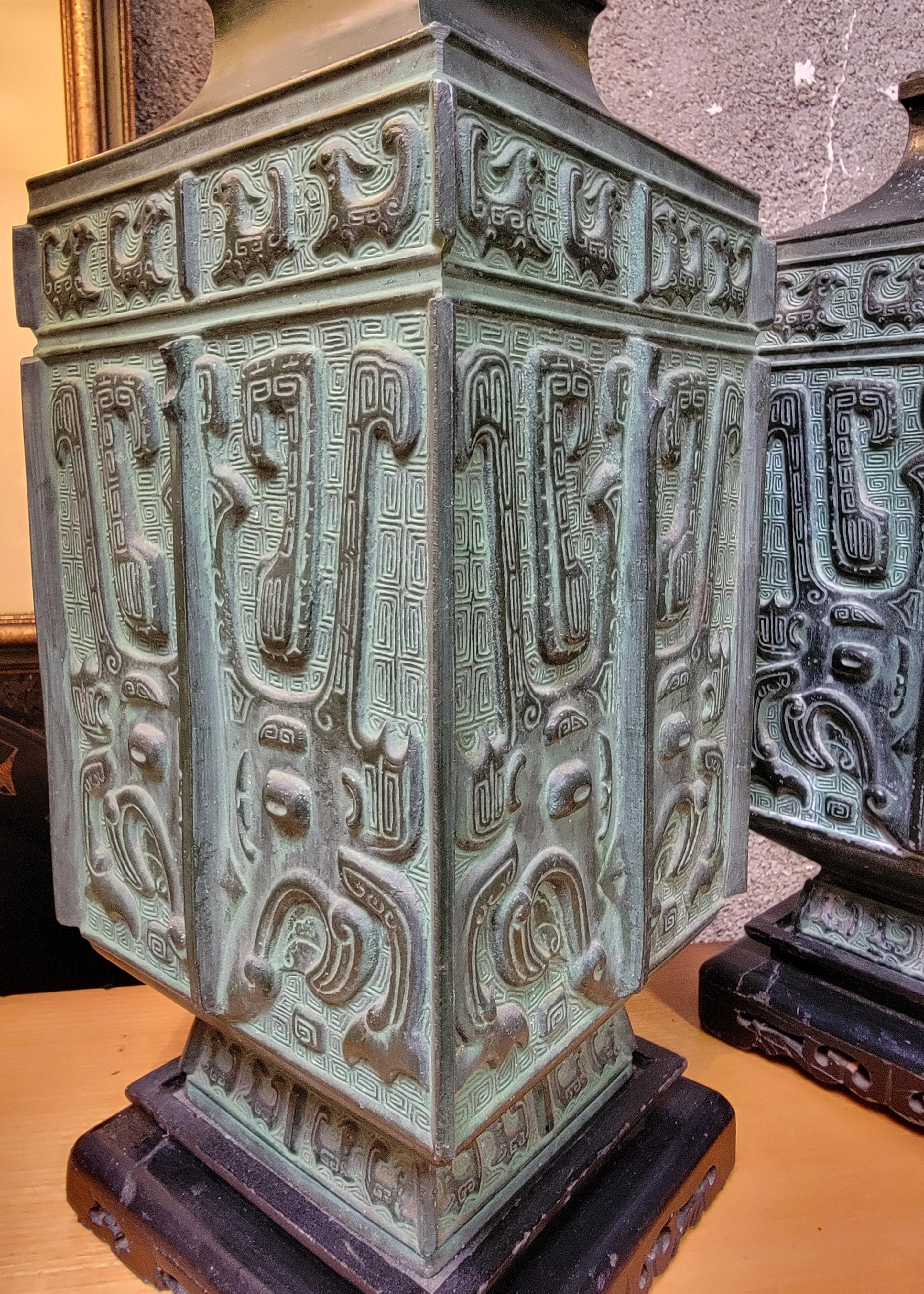 A unique pair of cast metal table lamps. They are heavy cast metal with a bronze like patina. Each lamp is mounted to an Asian style wood base. The design appears to be similar to a hieroglyphic pattern or possibly an Asian design. Pattern is on all