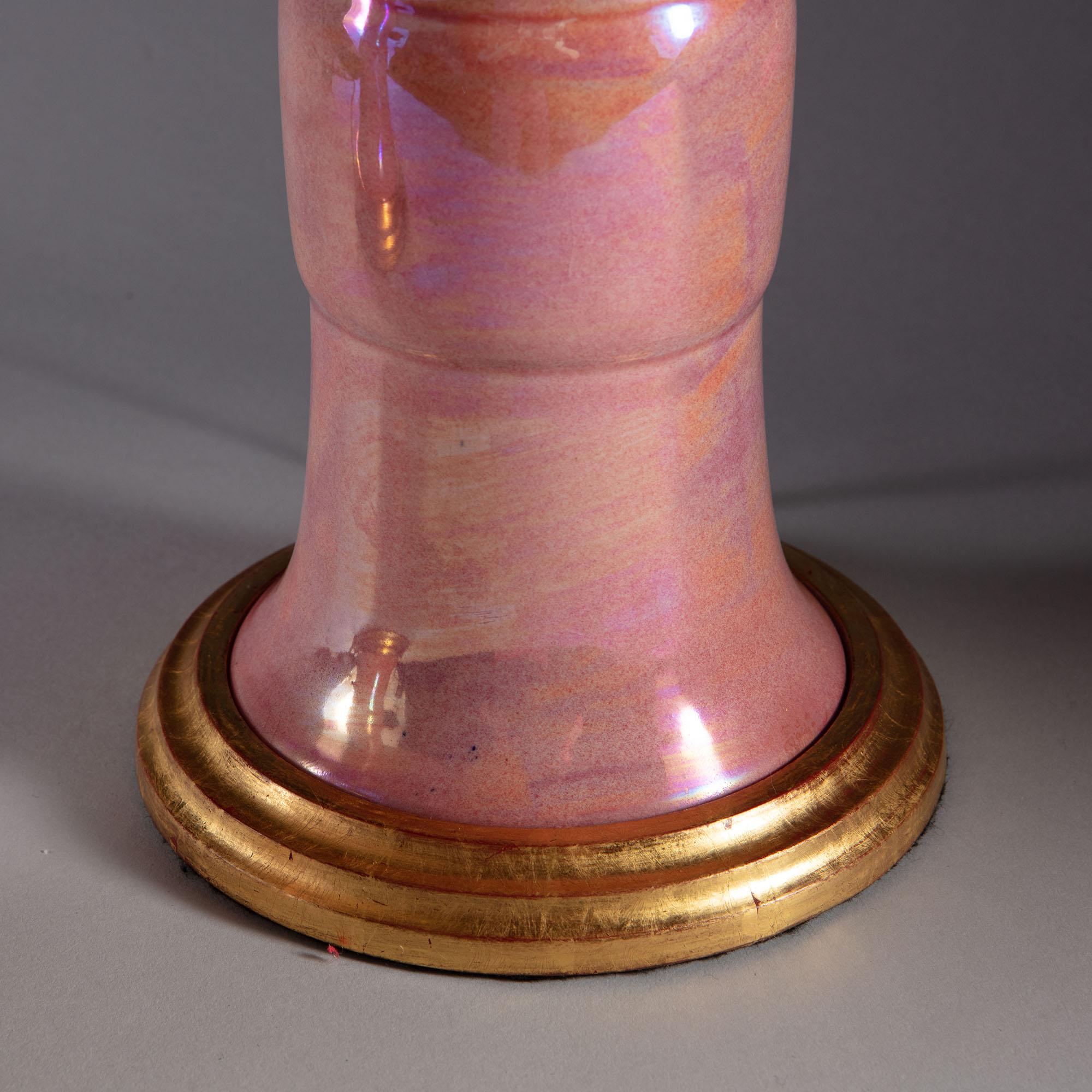 A pair of wonderfully kitsch pink iridescent luster glazed vases with gilt edges of classical Chinese vase form now mounted as table lamps on turned water gilt bases.

Measures: Height to top of vase 30cm 11 3/4in

Shades available separately