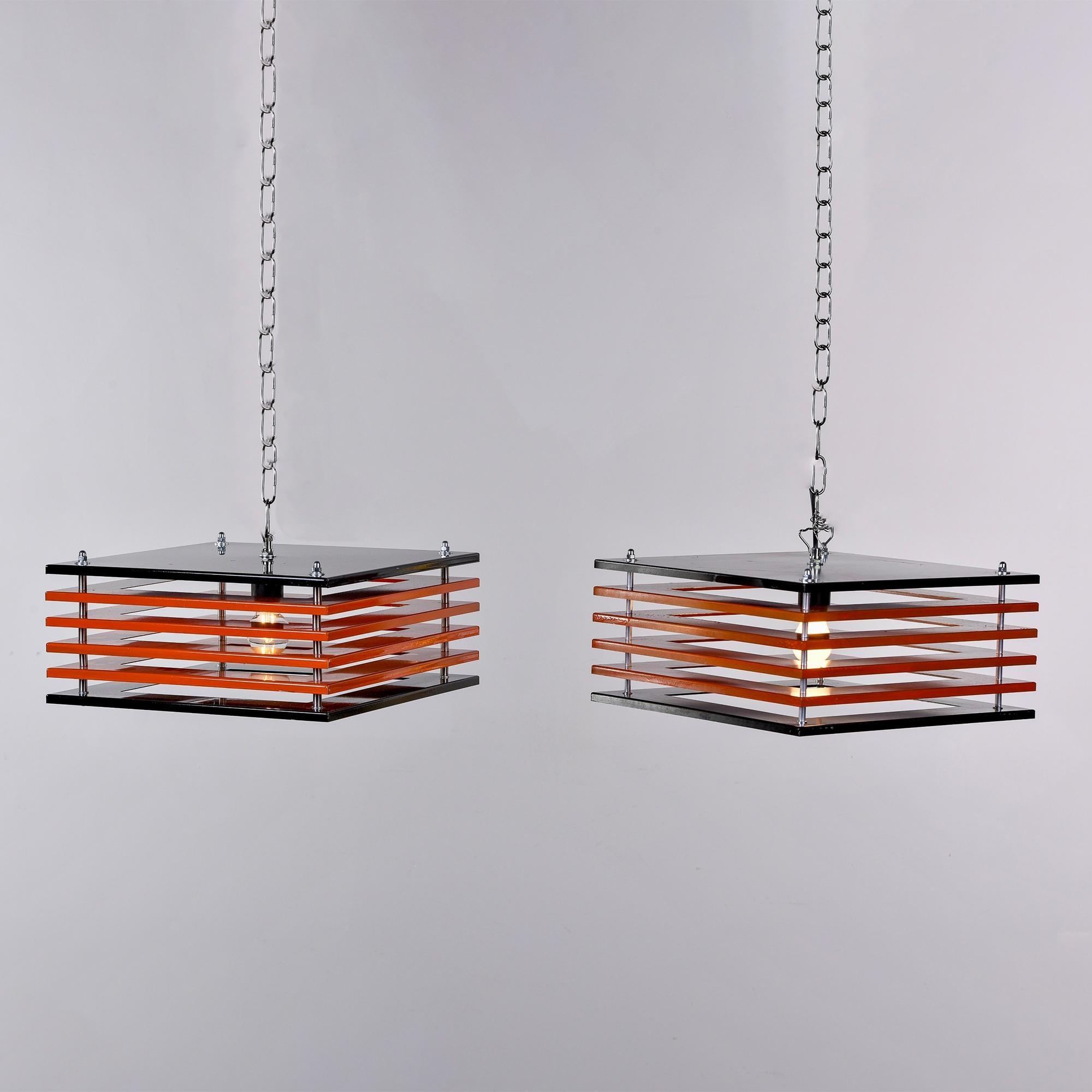 Found in Italy, this pair of mid century metal pendant lights dates from 1970. Each pendant has a single, standard sized socket and square shaped frame that has a black top and bottom with stacks of four orange disks between. Unknown maker. New