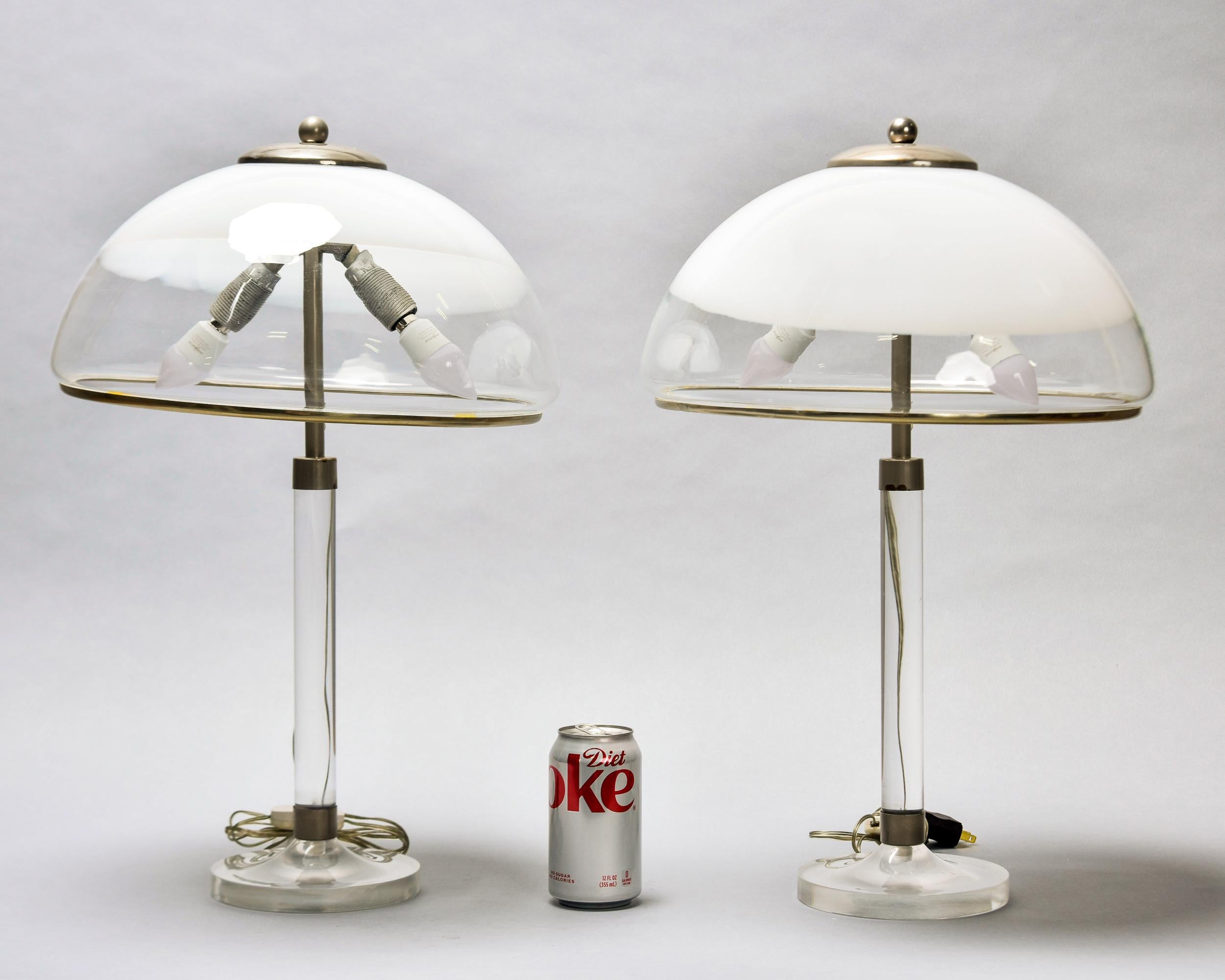 Trouvée en Italie, cette paire de lampes de table inhabituelle date des années 1970. Chaque lampe est composée d'une base et d'une colonne de support en Lucite clair avec deux douilles de taille candélabre, surmontées d'abat-jours en verre clair