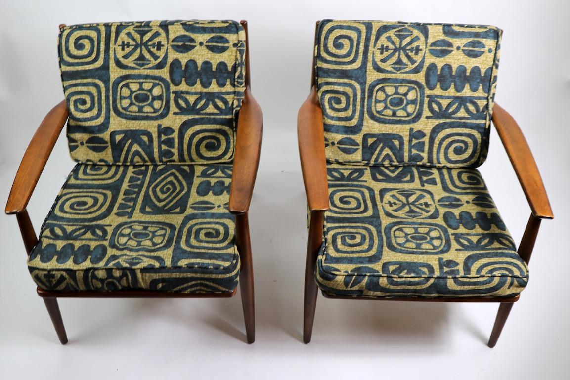 Pair of open arm lounge chairs by Baumritter, with solid beech and ash frames, and original cushions, cushions show wear. Both are in very good original condition, we have replaced the straps which support the seat cushions. Frames are nice and