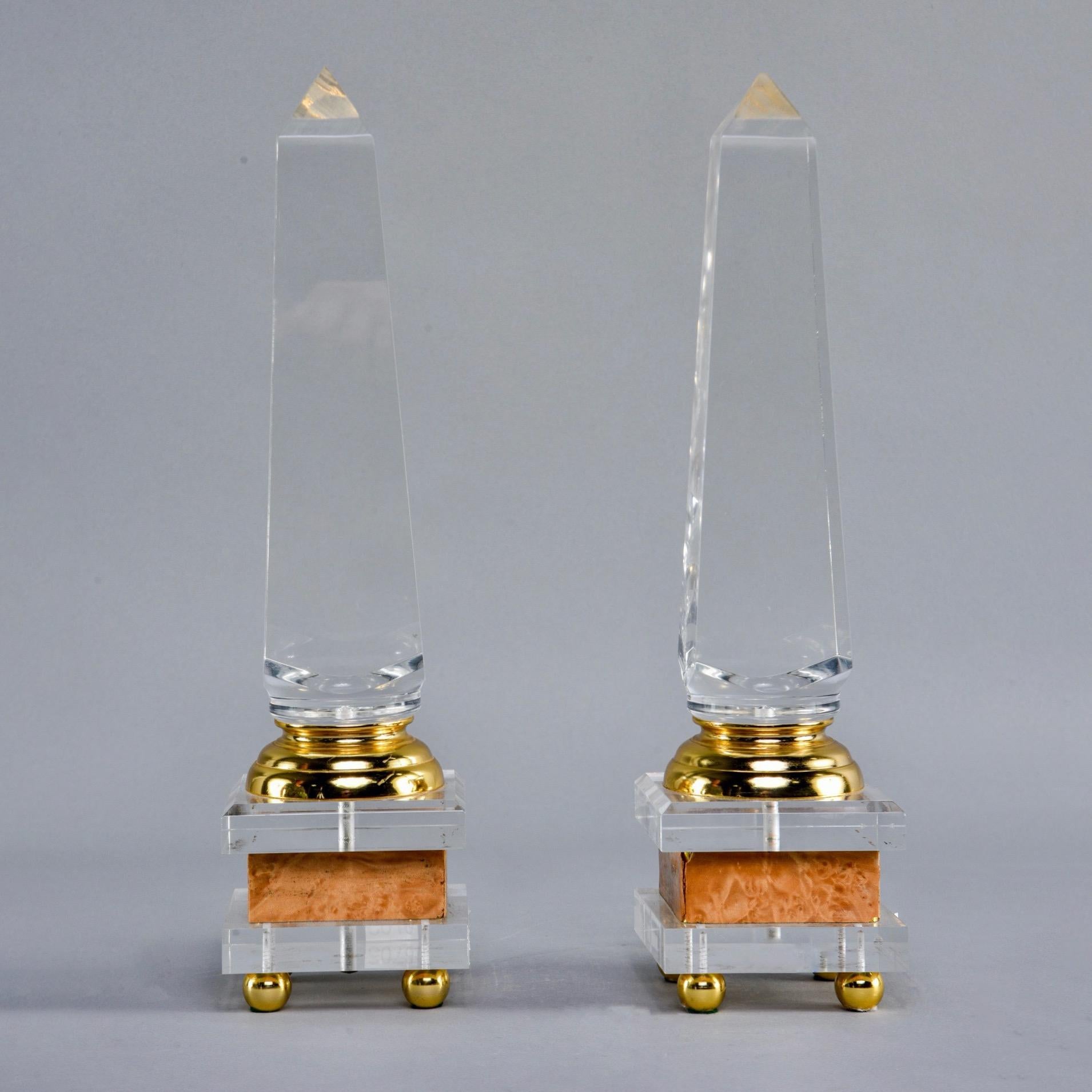 Pair of decorative Lucite and brass footed obelisks in manner of Maison Jansen, circa 1980s. Found in France. Unknown maker. Base has round brass feet, faux stone band and brass accents. This pair stands just over 15” tall. At the time of this